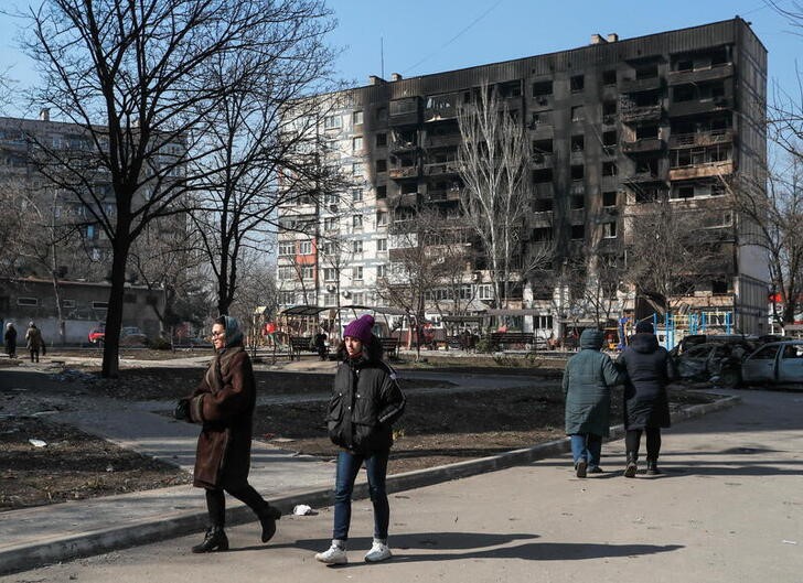 People walk in front of a building damaged in fighting during Ukraine-Russia conflict, in the besieged southern port of Mariupol