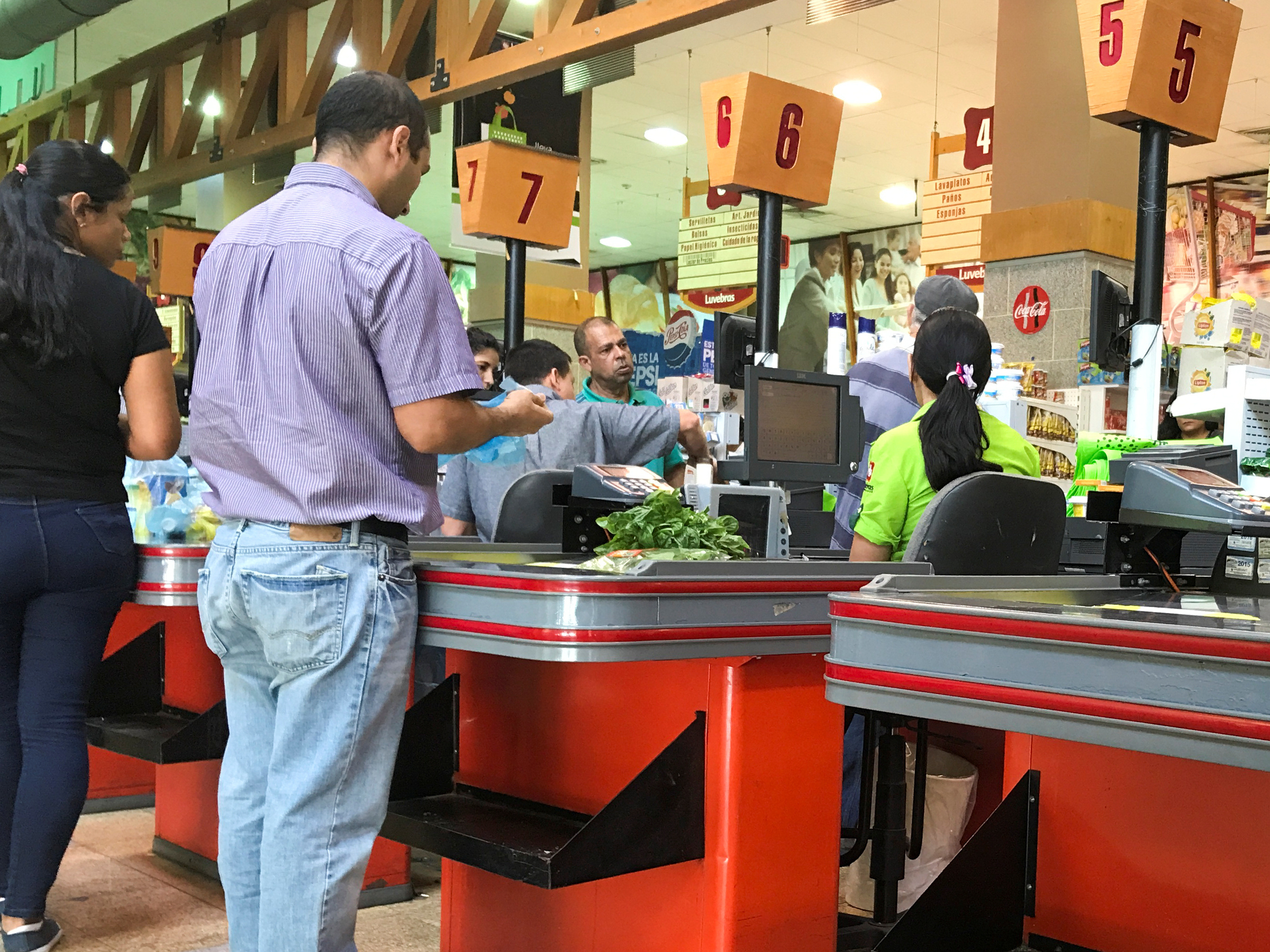 People queue to pay for food at the cashier of a supermarket in Caracas