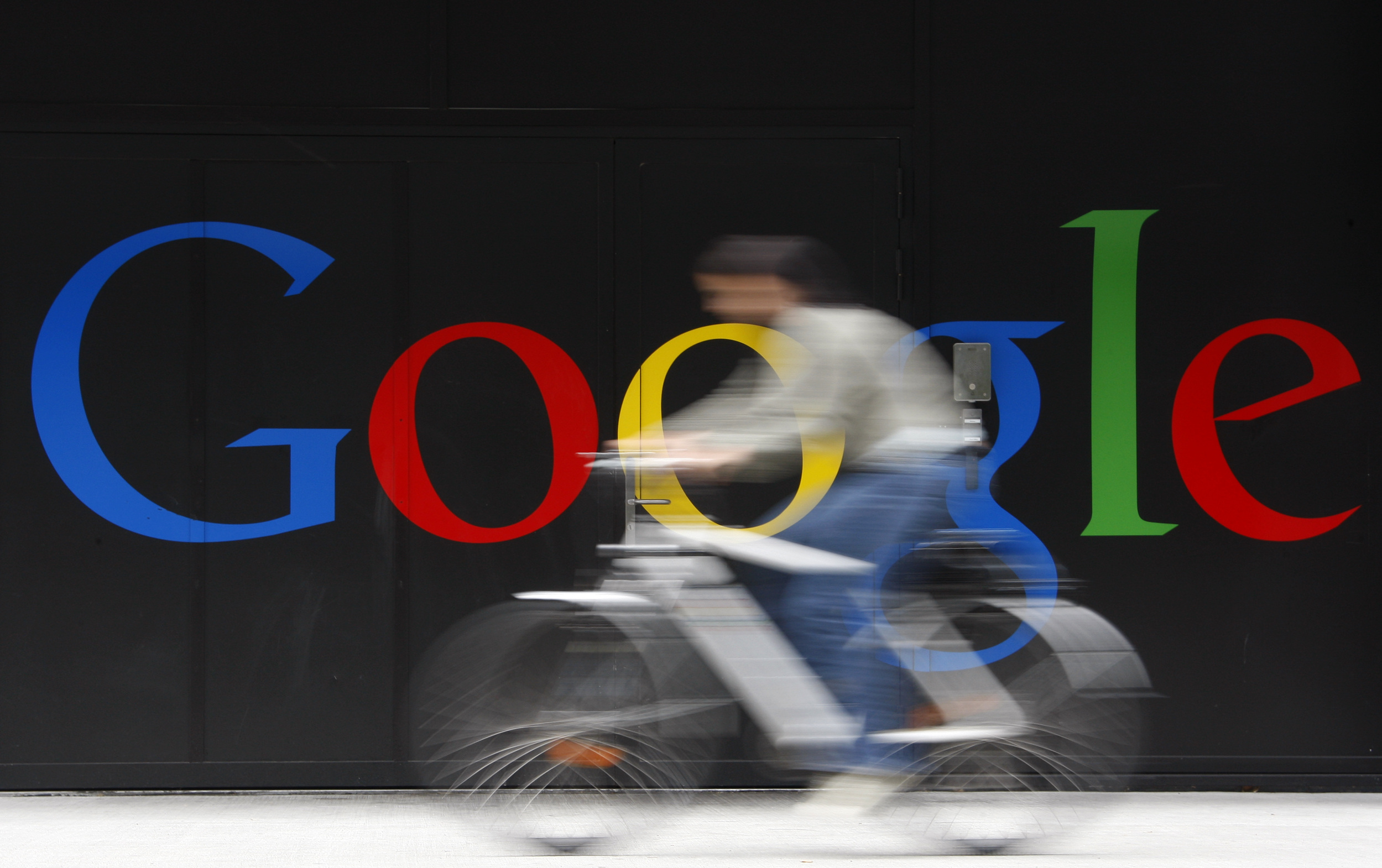 An employee rides her bike past a logo next to the main entrance of a Google building