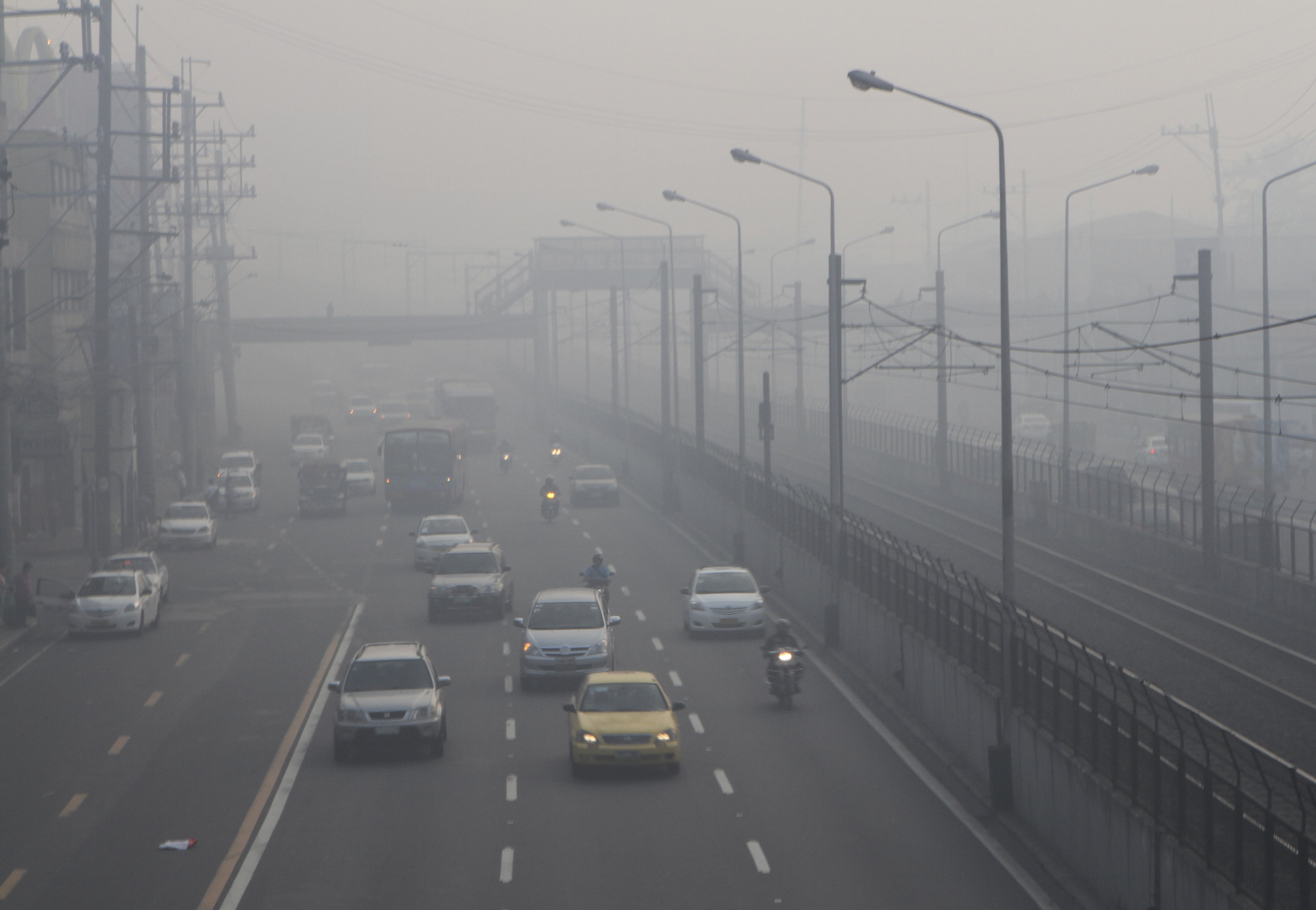 Motorists switch on their headlights while crossing a highway covered by smog in Manila