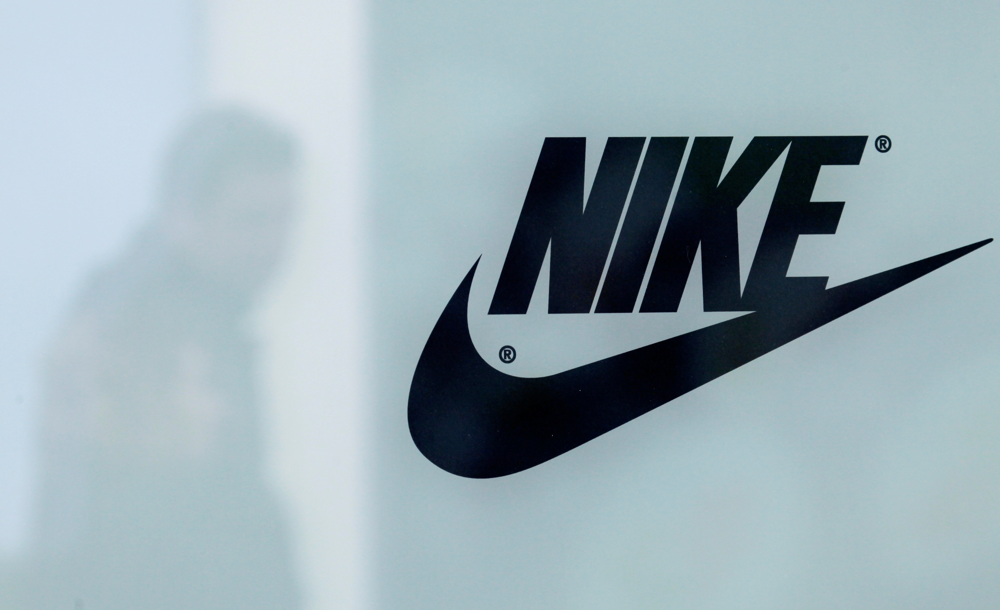 A customer is reflected in a shop window decorated with Nike store logo at the outlet village Belaya Dacha outside Moscow