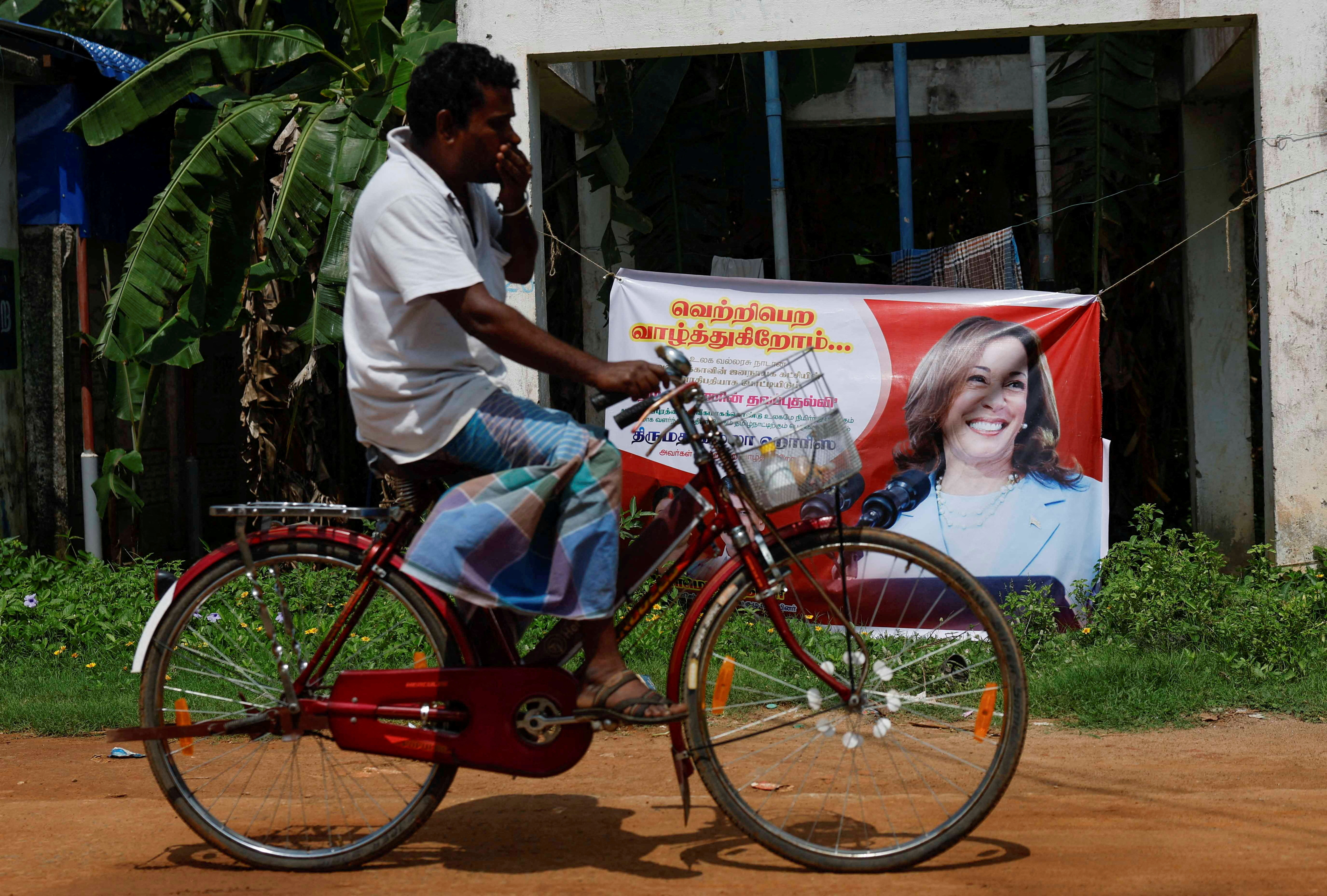 A man cycles past a poster of Democratic presidential nominee U.S. Vice President Kamala Harris in Thulasendrapuram