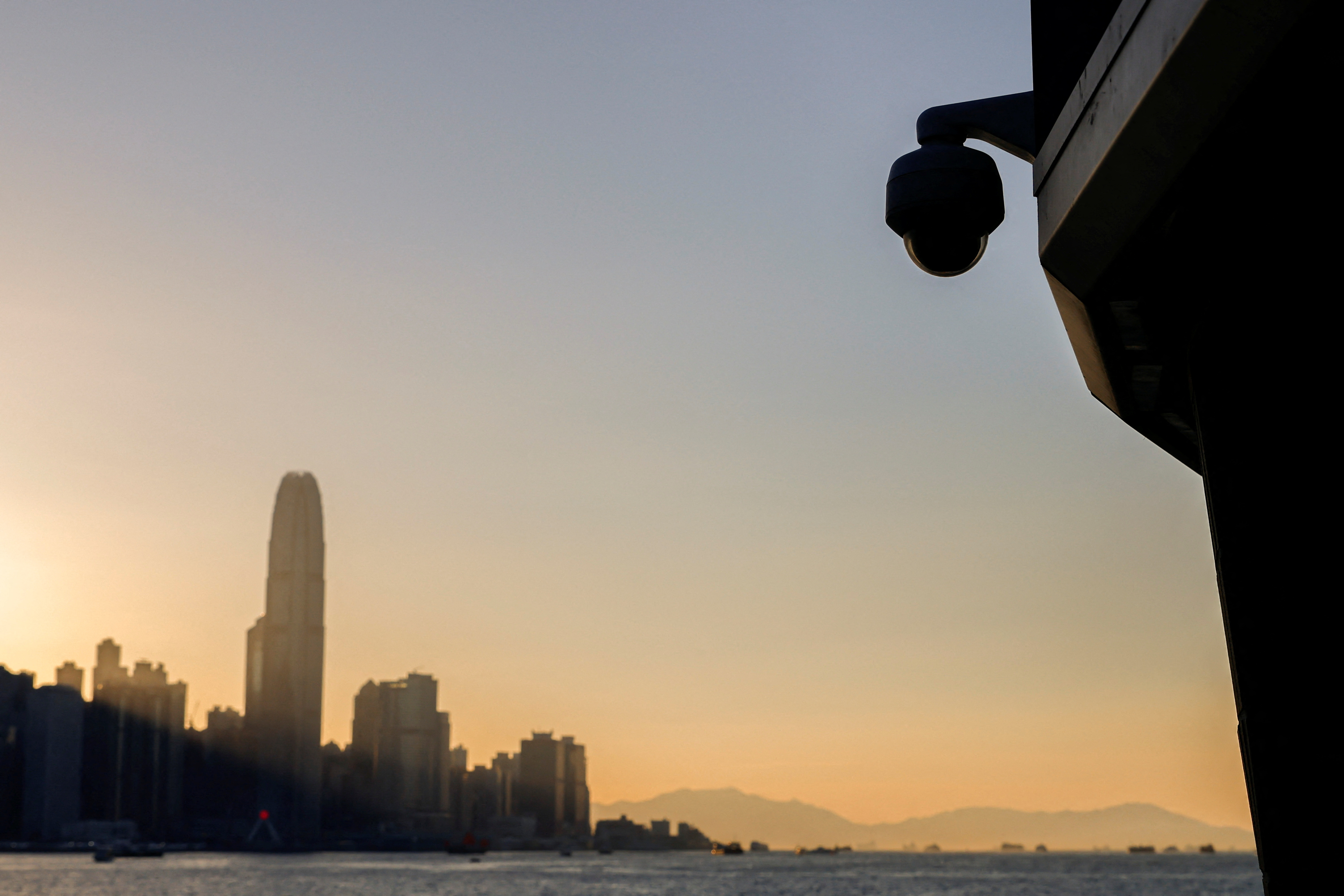 A surveillance camera is seen by the waterfront as skyline buildings stand across Victoria Harbor, in Hong Kong