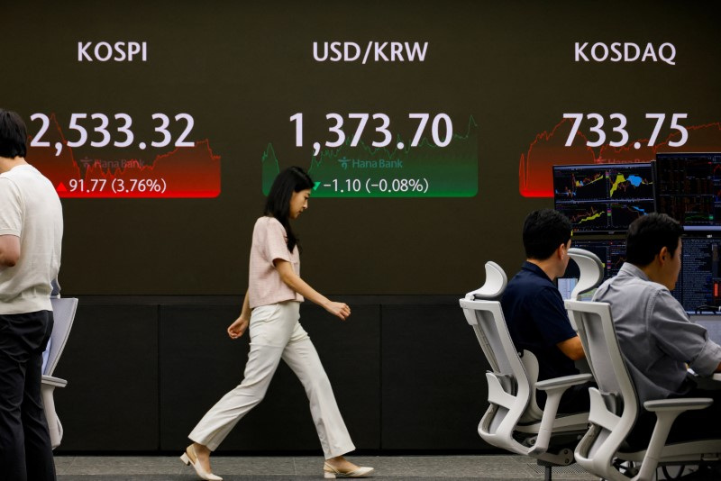 A currency dealer walks in front of an electronic board showing KOSPI in the dealing room of a bank, in Seoul