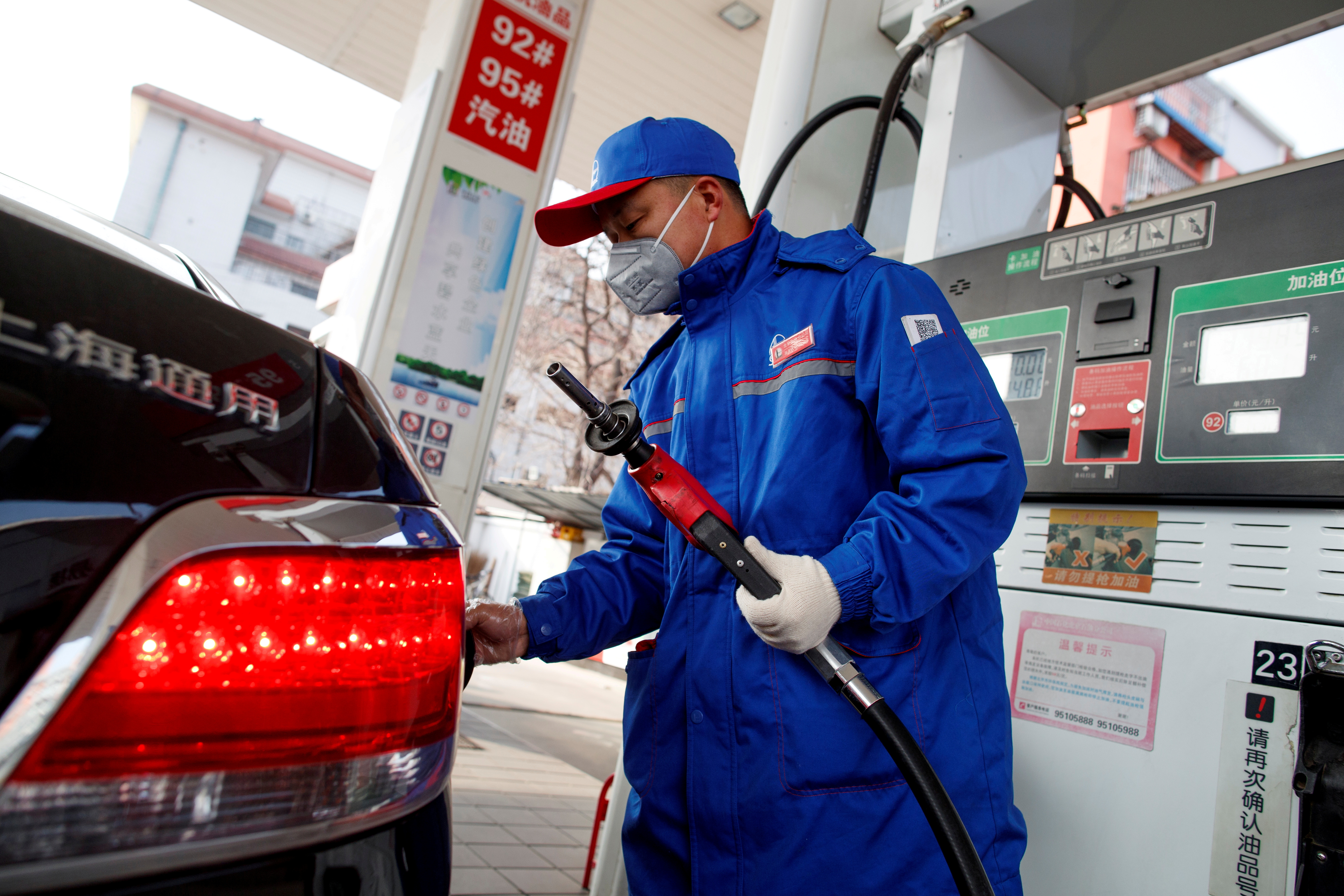 A pump attendant wears a mask as he refuels a car at a Sinopec gas station in Beijing