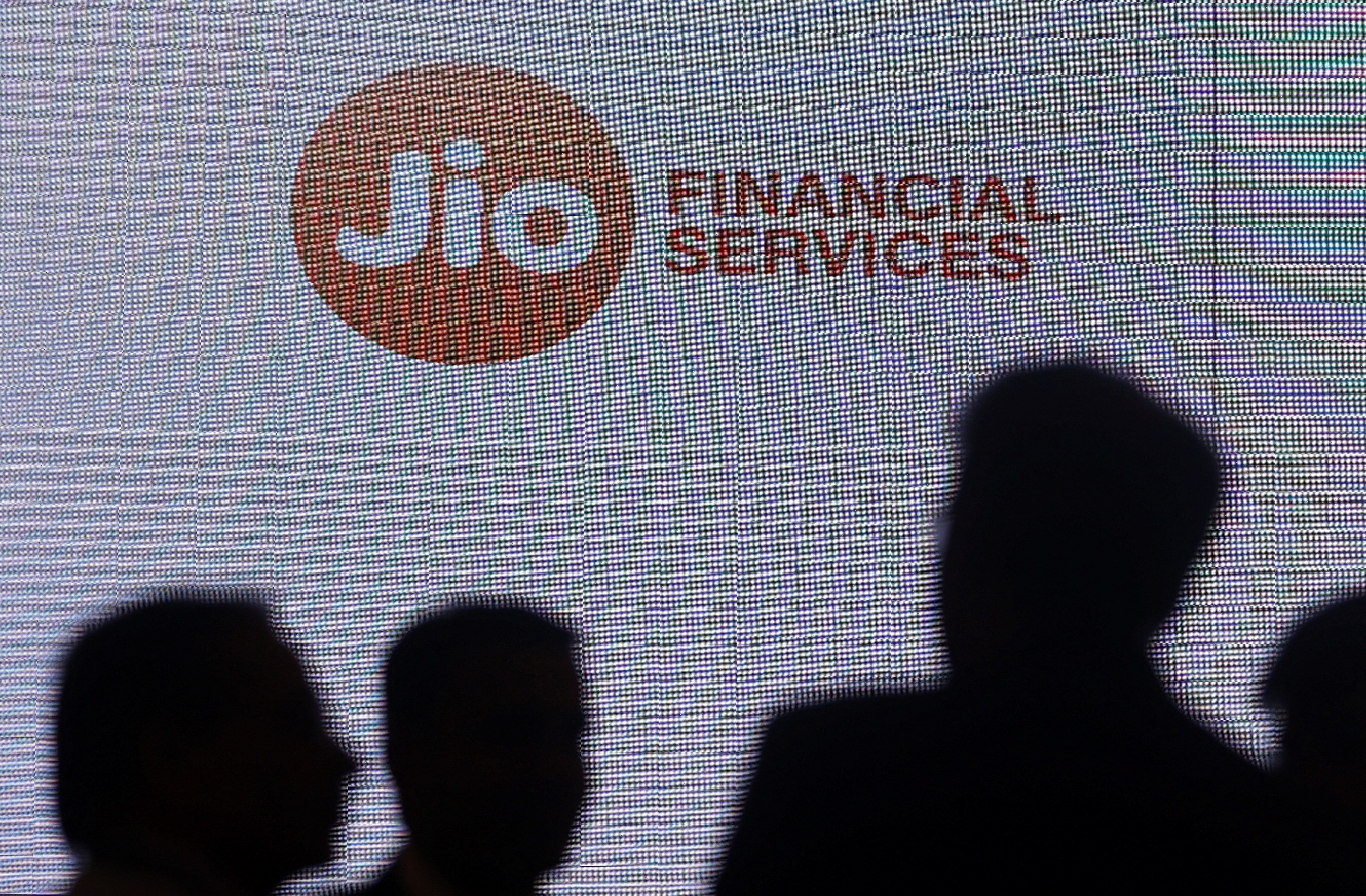 People stand next to a logo of Jio Financial Services ahead of its listing ceremony at the Bombay Stock Exchange in Mumbai