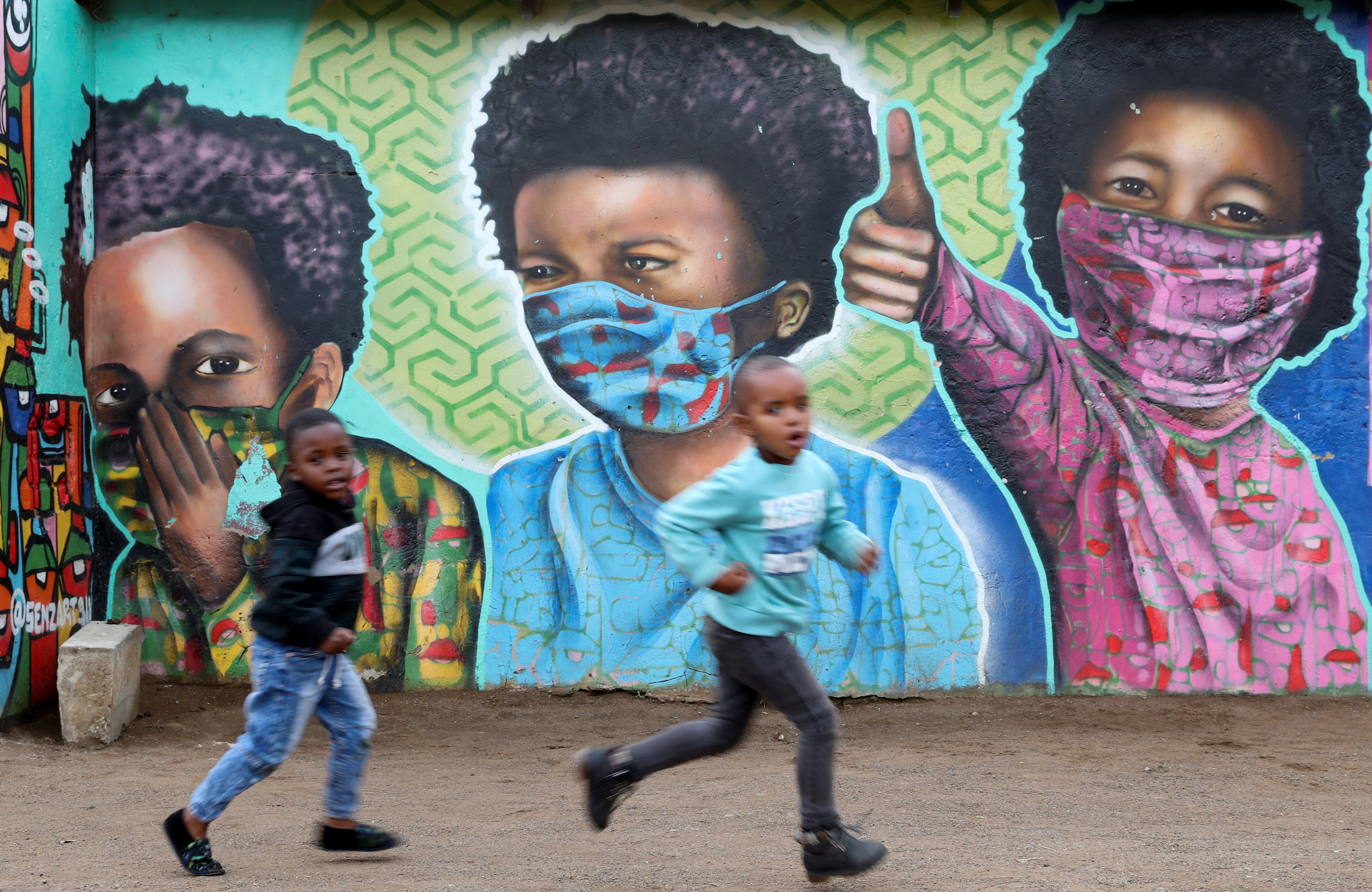 Boys run past a mural by Senzart911, of children wearing facemasks