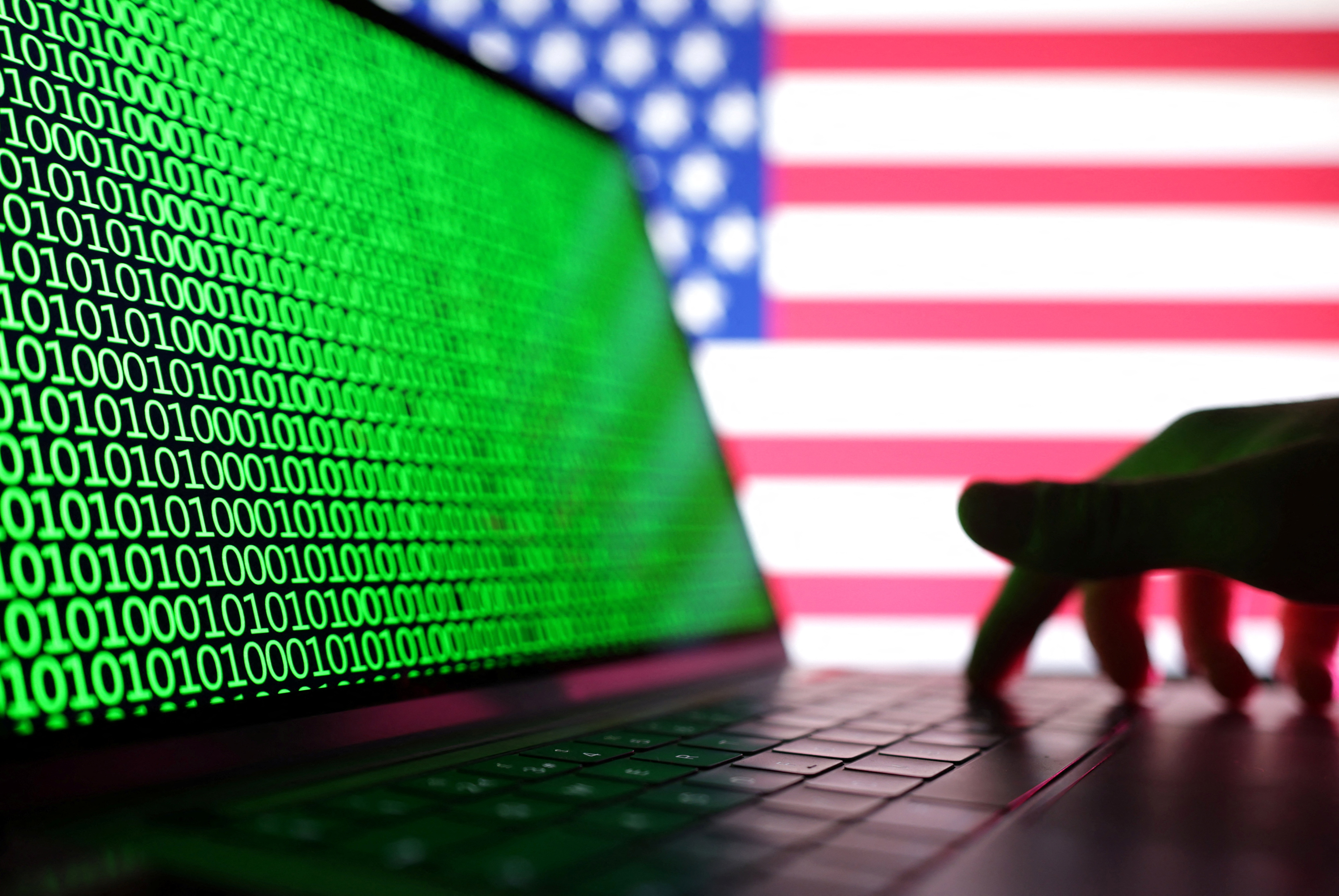 Illustration shows a laptop with binary codes displayed in front of the USA flag