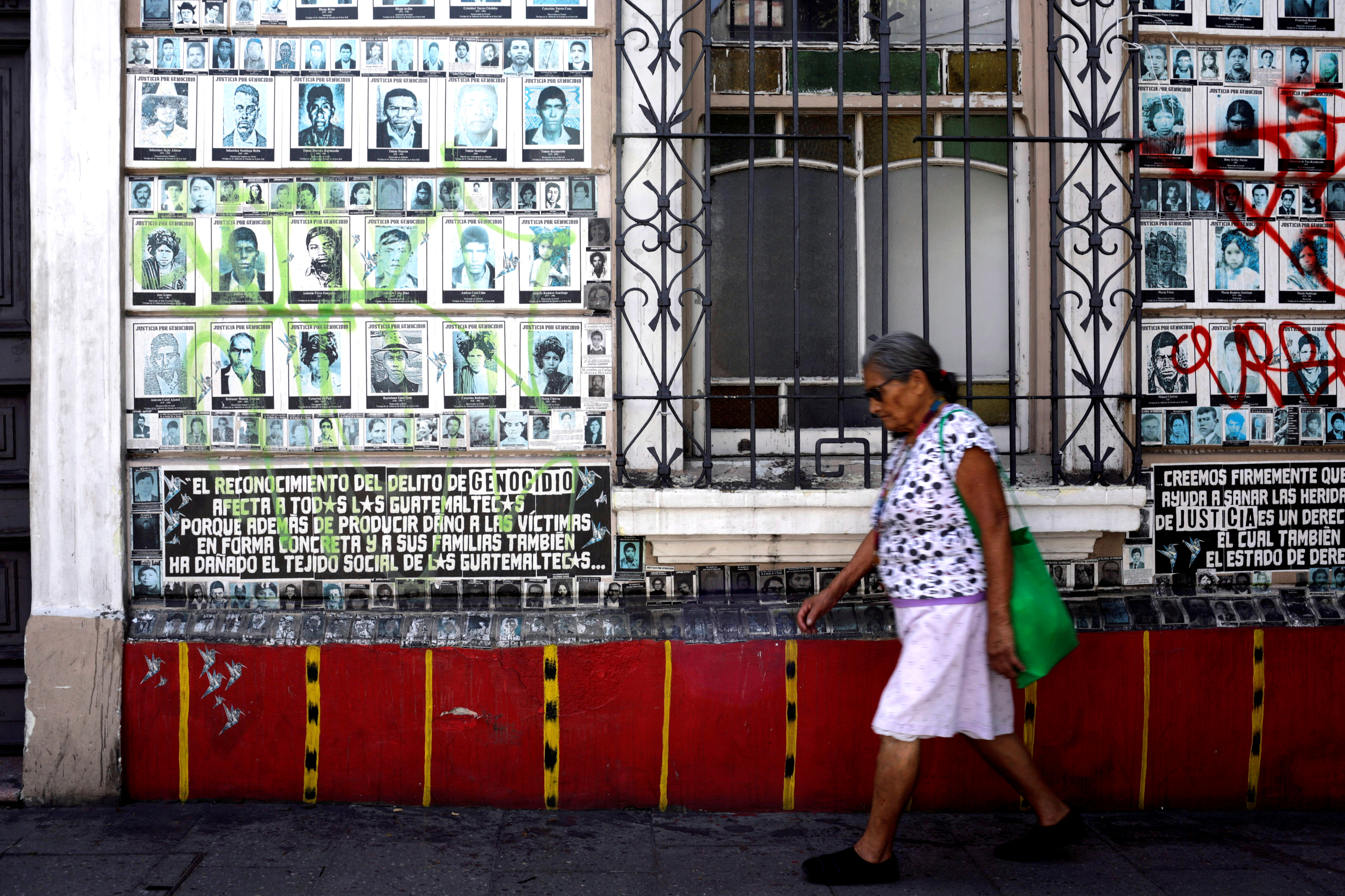 A woman walks in front of a wall with images of people disappeared during the Guatemala civil war ahead of Sunday's presidential election in Guatemala City