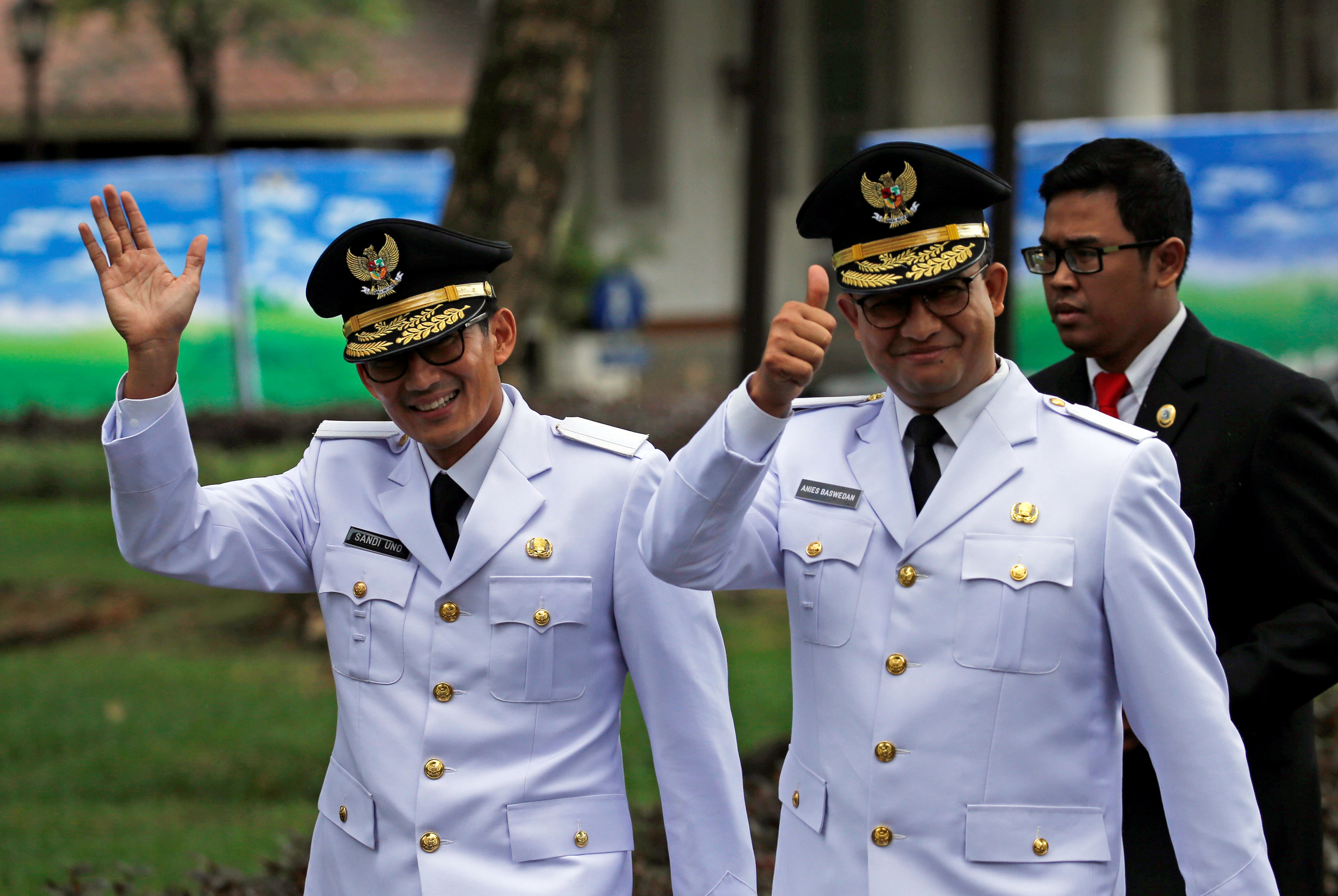 Jakarta Governor Anies Baswedan and his deputy Sandiaga Uno wave to reporters before a swearing-in at the Presidential Palace in Jakarta