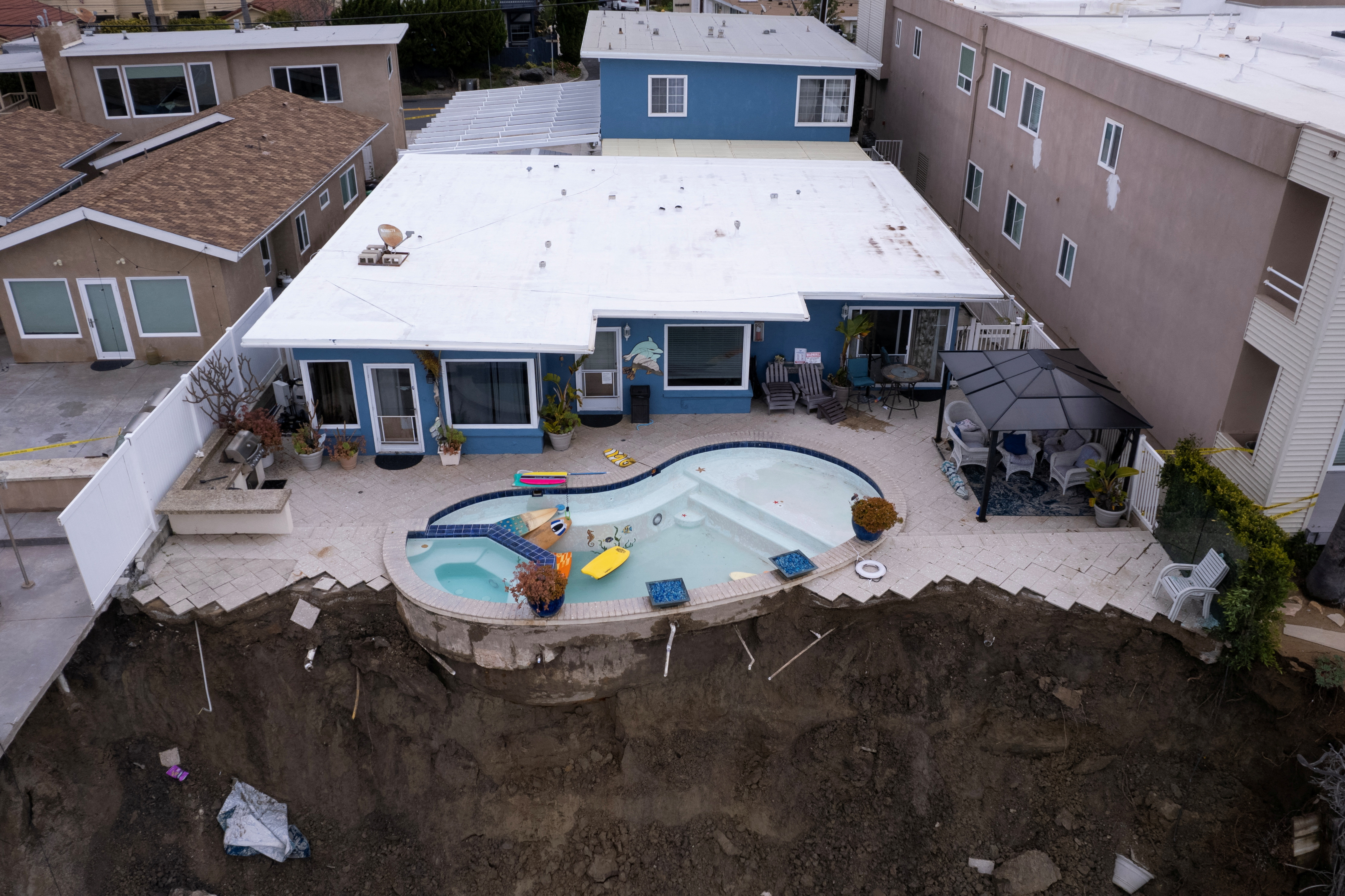 A backyard pool hangs on cliffside after torrential rains hits California beachtown