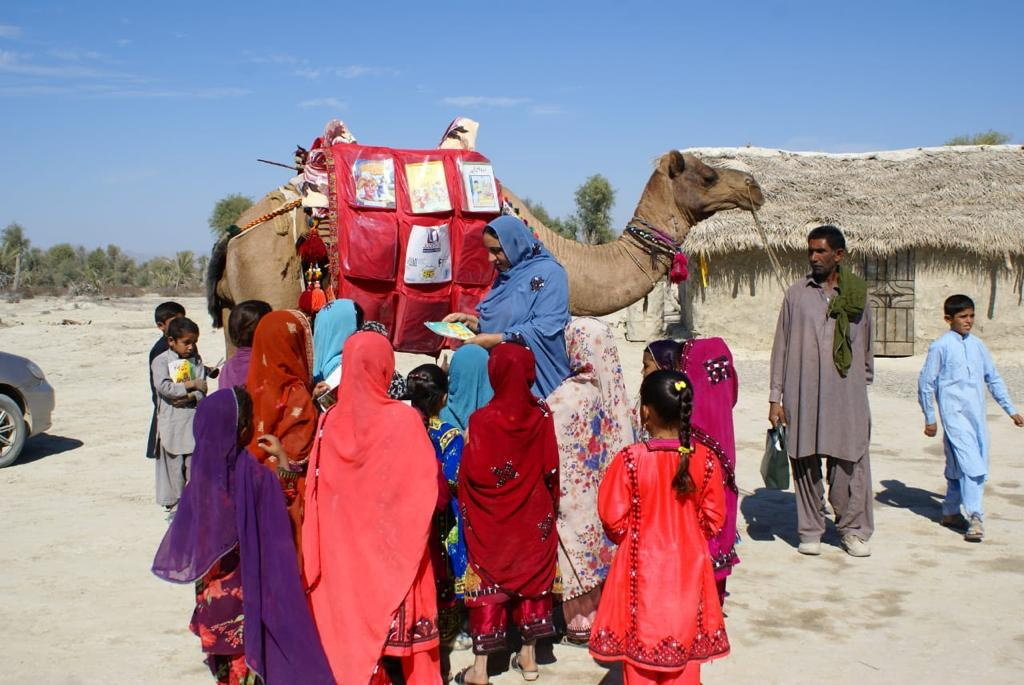 Children stand next to a camel that brought books in Mand