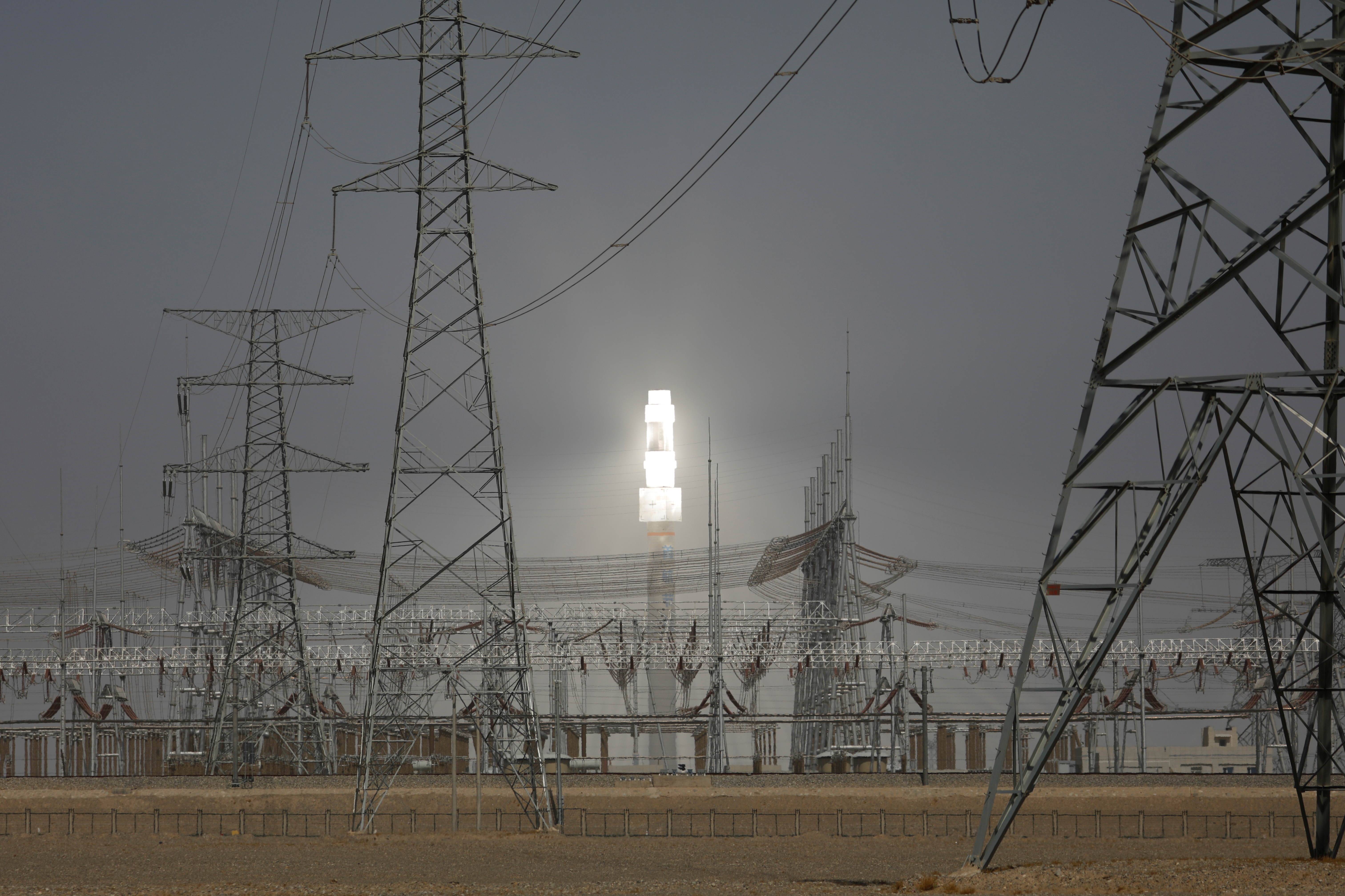 A molten salt solar tower stands behind electricity pylons at a power station near Dunhuang