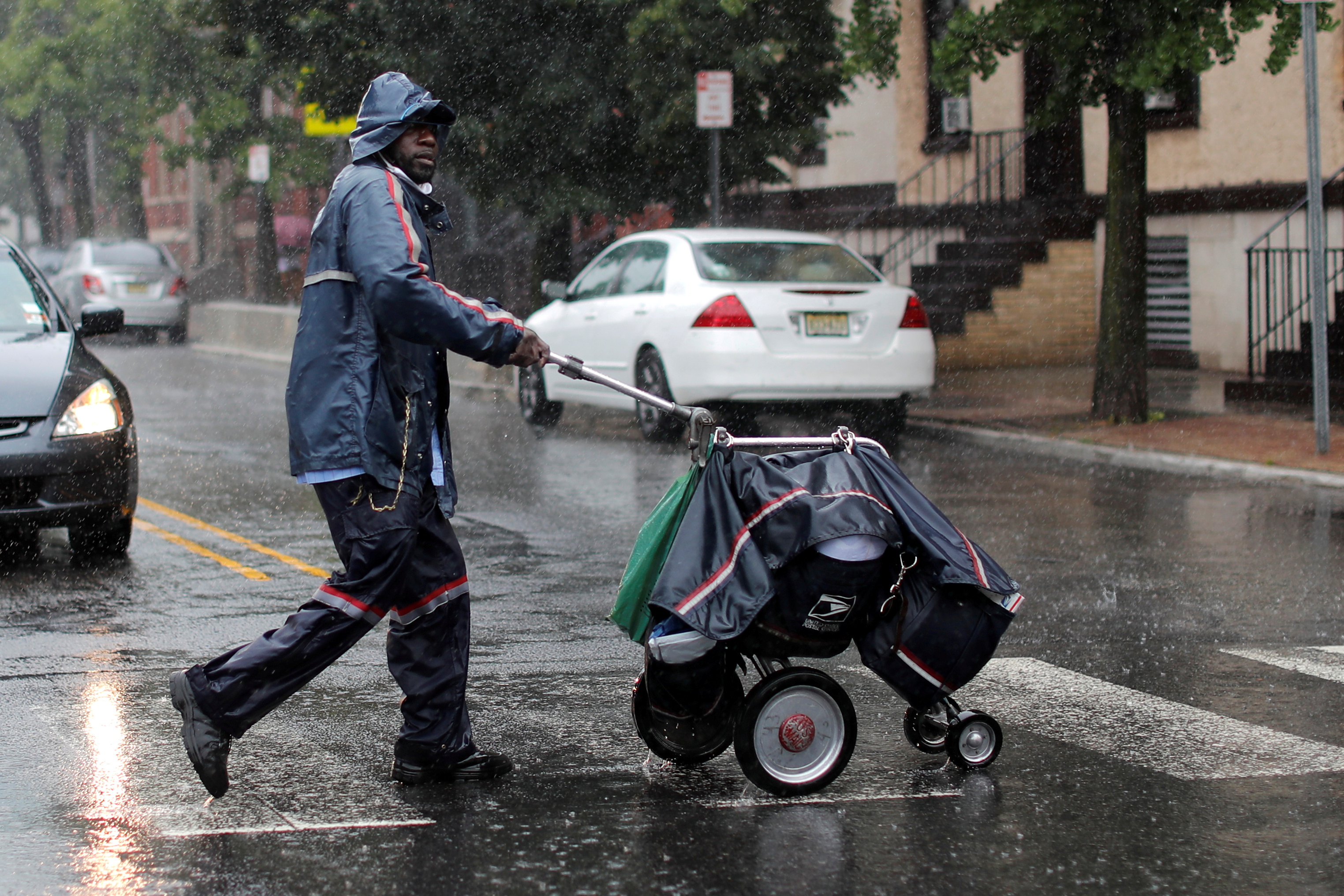 A United States Postal Service (USPS) mail carrier walks through heavy rain in Jersey City, New Jersey, U.S., July 10, 2020. REUTERS/Mike Segar/File Photo