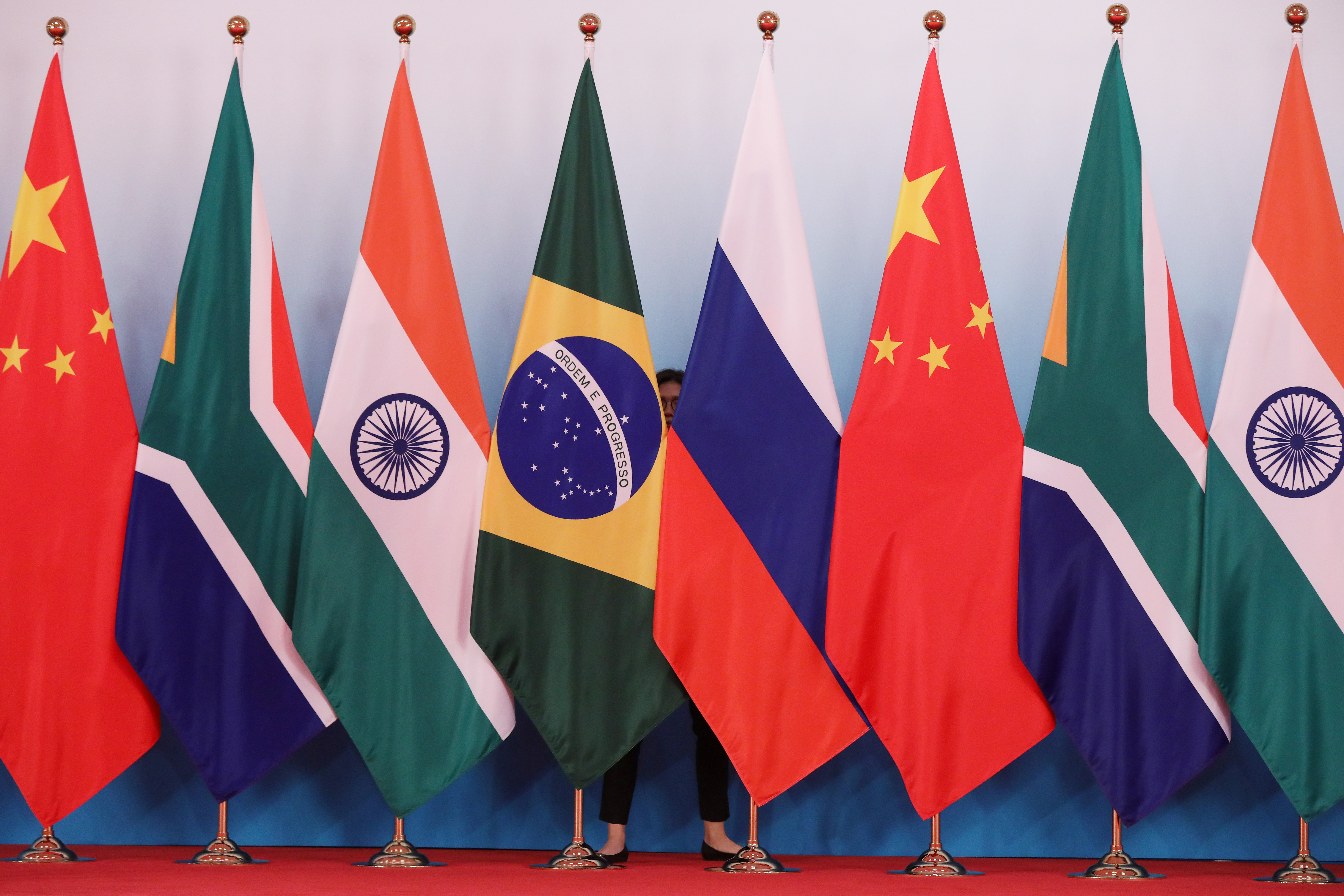 A staff worker stands behind the national flags of Brazil, Russia, China, South Africa and India to tidy the flags before a group photo during the BRICS Summit in Xiamen