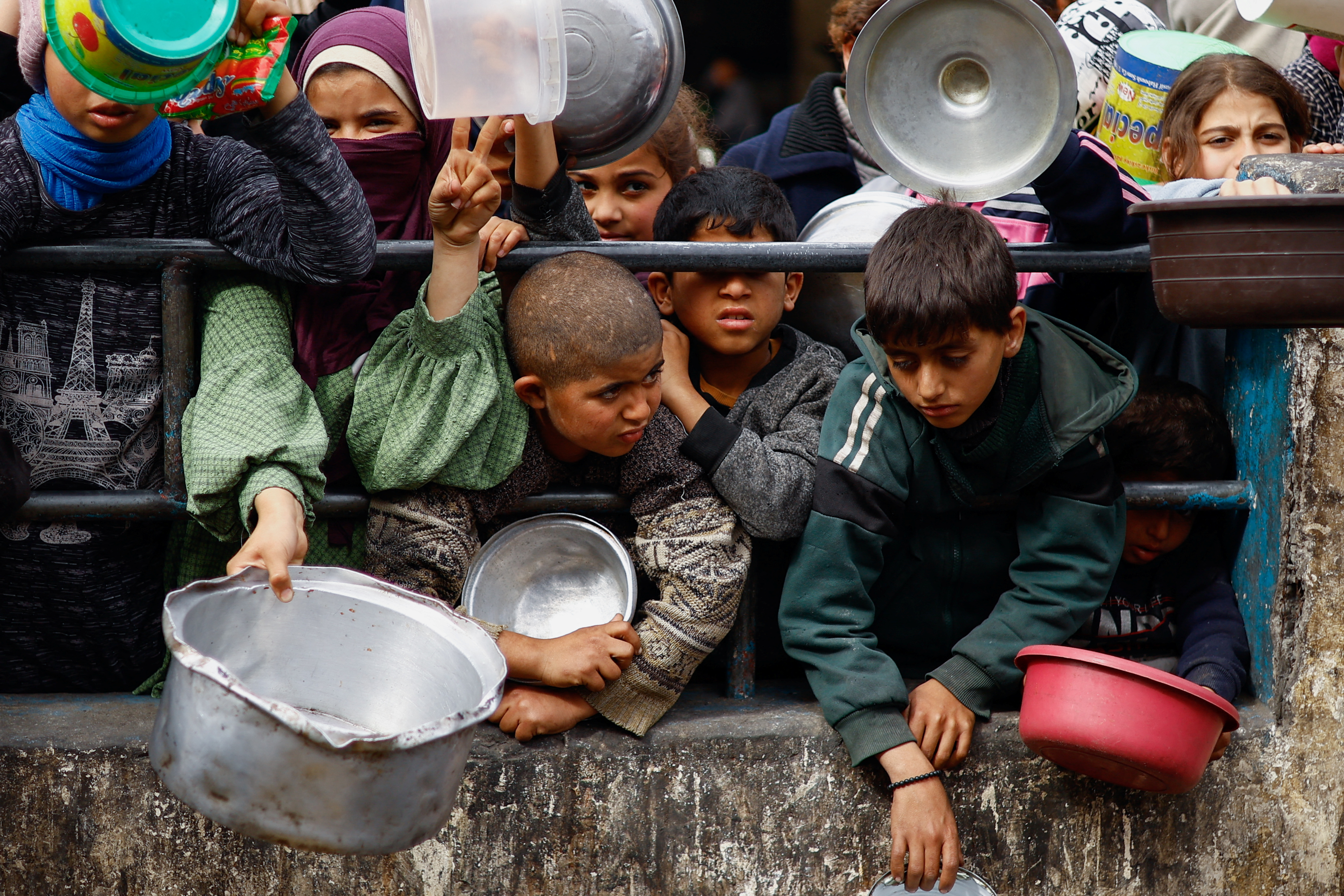 Palestinian children wait to receive food cooked by a charity kitchen amid shortages of food supplies, in Rafah