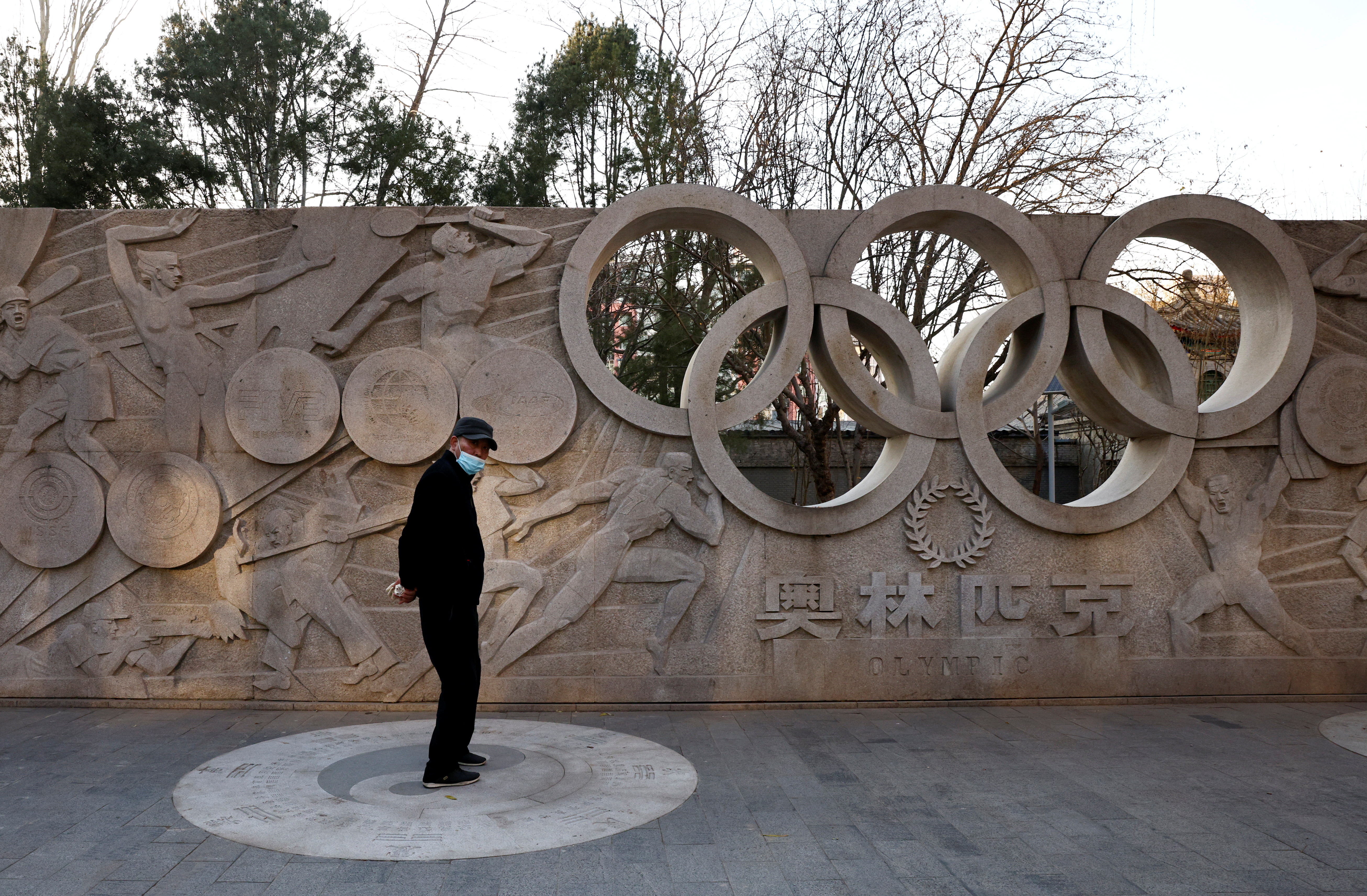 Man stands in front of a base relief containing the Olympic Rings in a park in Beijing as the city prepares for the 2022 Olympics
