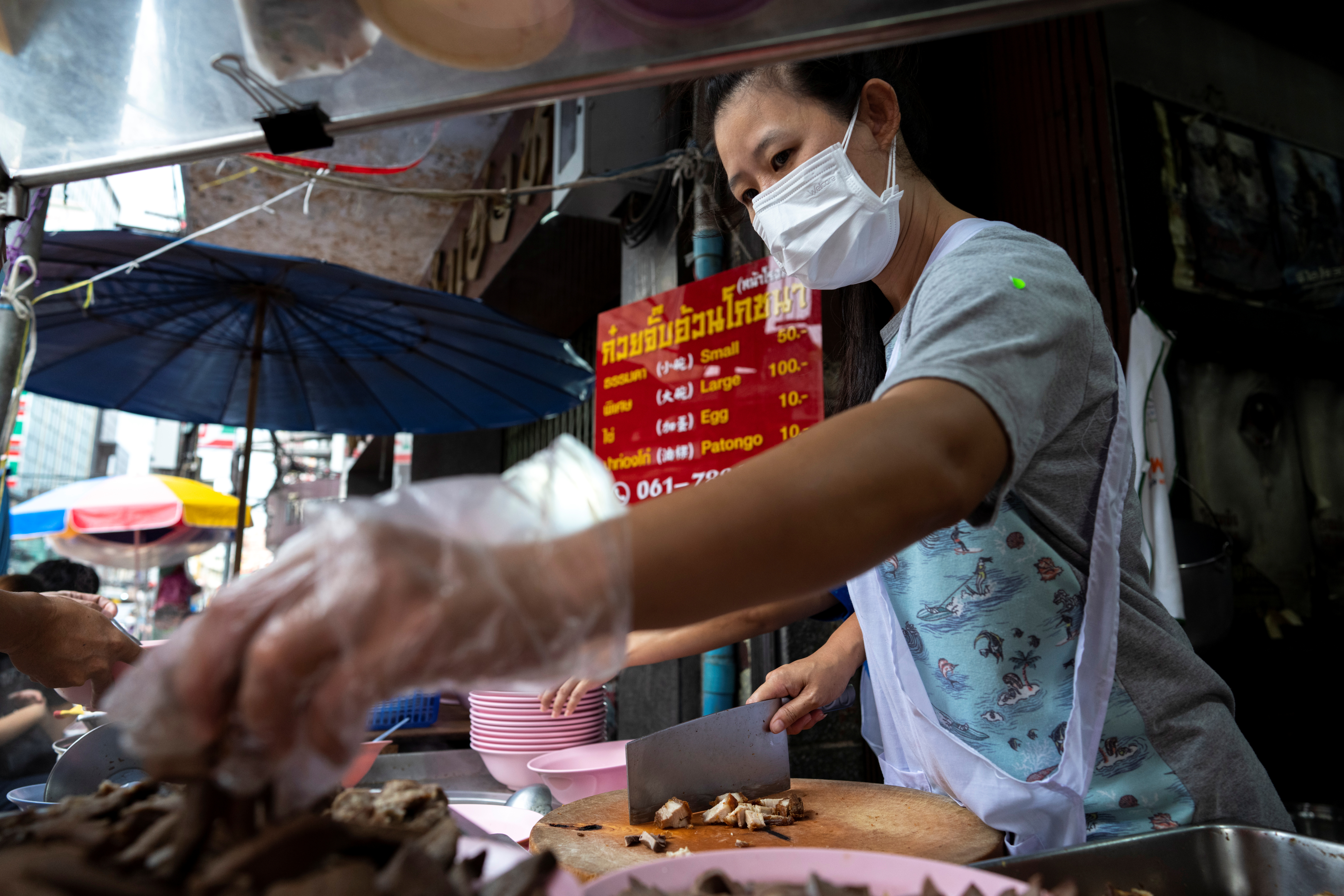 Jirintat Tangsupmanee, 45, wearing a face mask and a plastic glove to prevent the spread of the coronavirus disease (COVID-19), cooks 