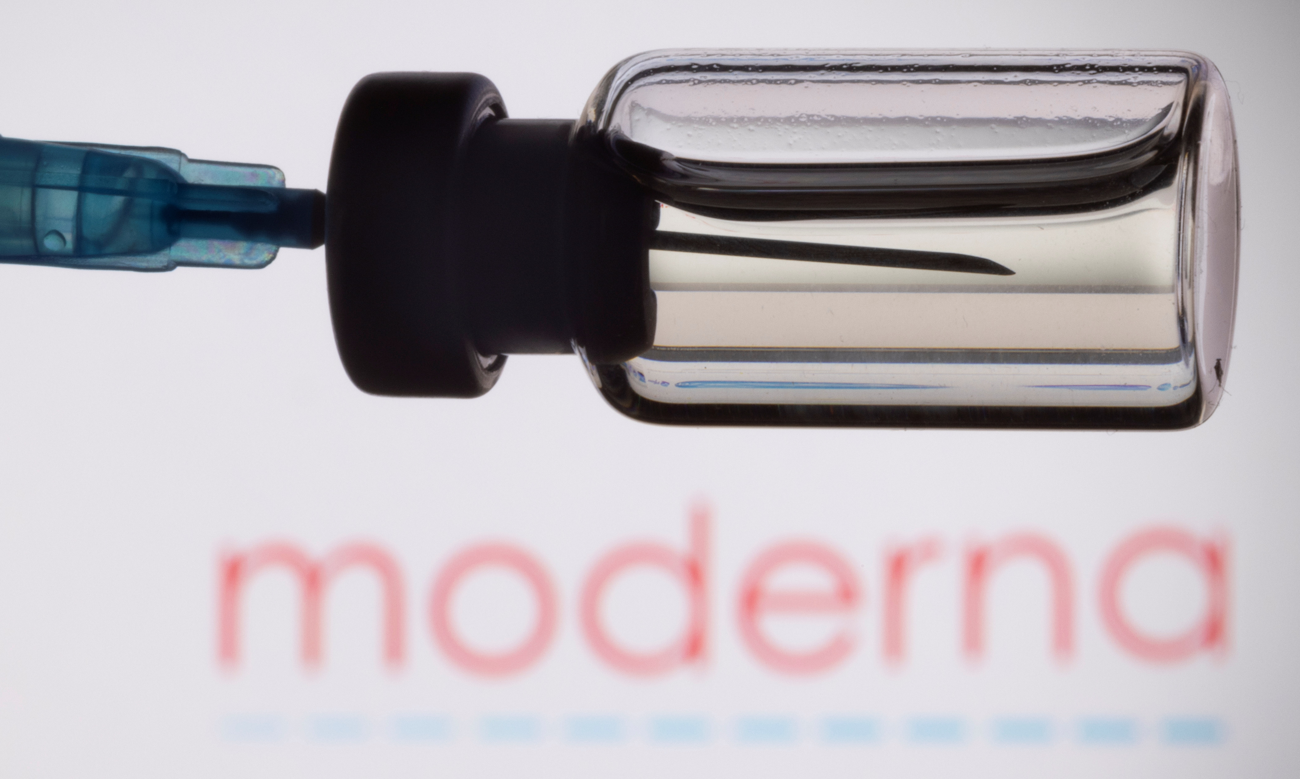 A vial and a syringe are seen in front of a displayed Moderna logo, in this illustration taken