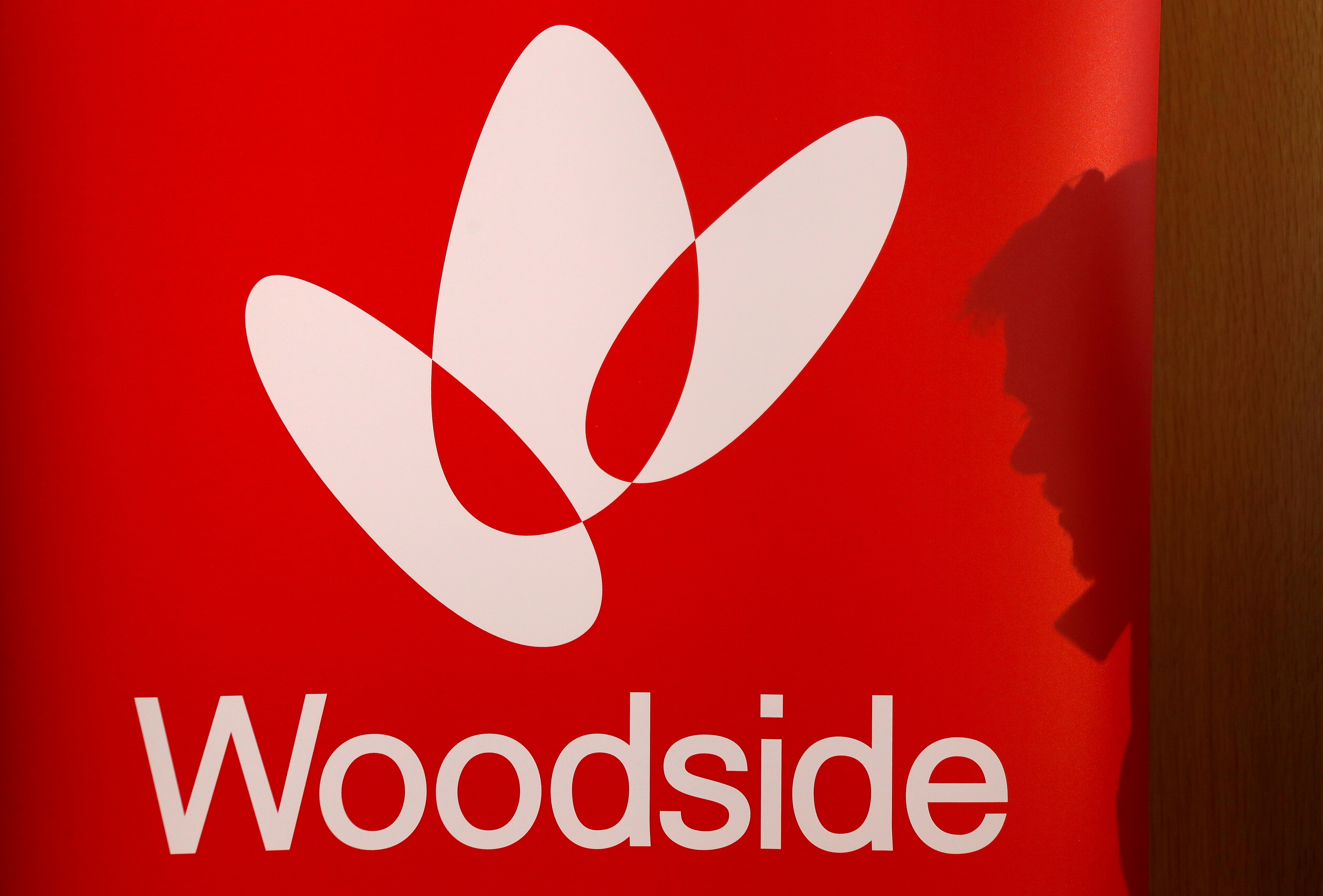 The shadow of a man is cast onto a poster displaying the logo for Australia's Woodside Petroleum