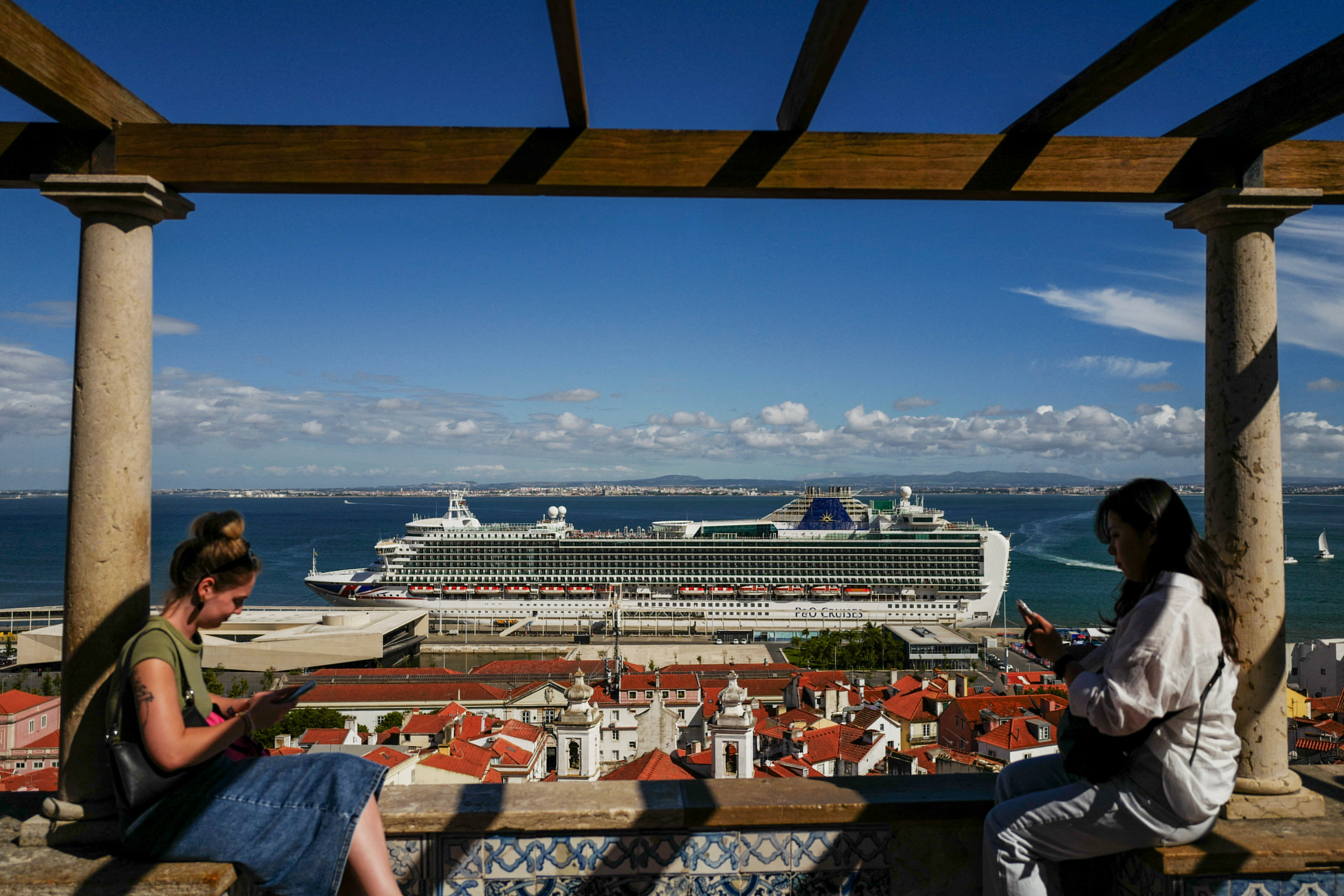 People stand in Santa Luzia viewpoint, while a cruise ship prepares to leave from the Cruise Port of Lisbon