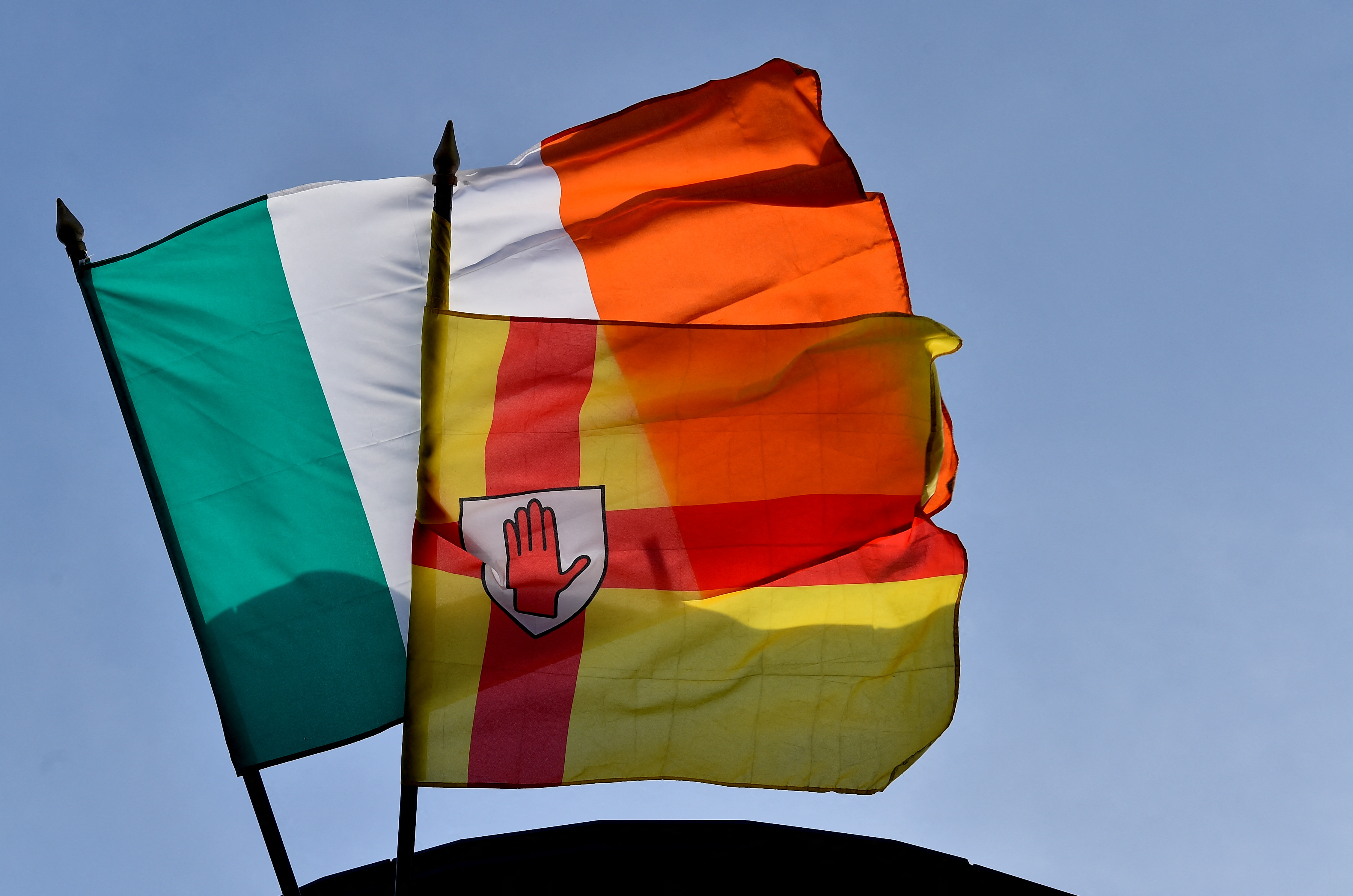 Irish and Ulster flags flutter in the wind on top of a building in Belfast