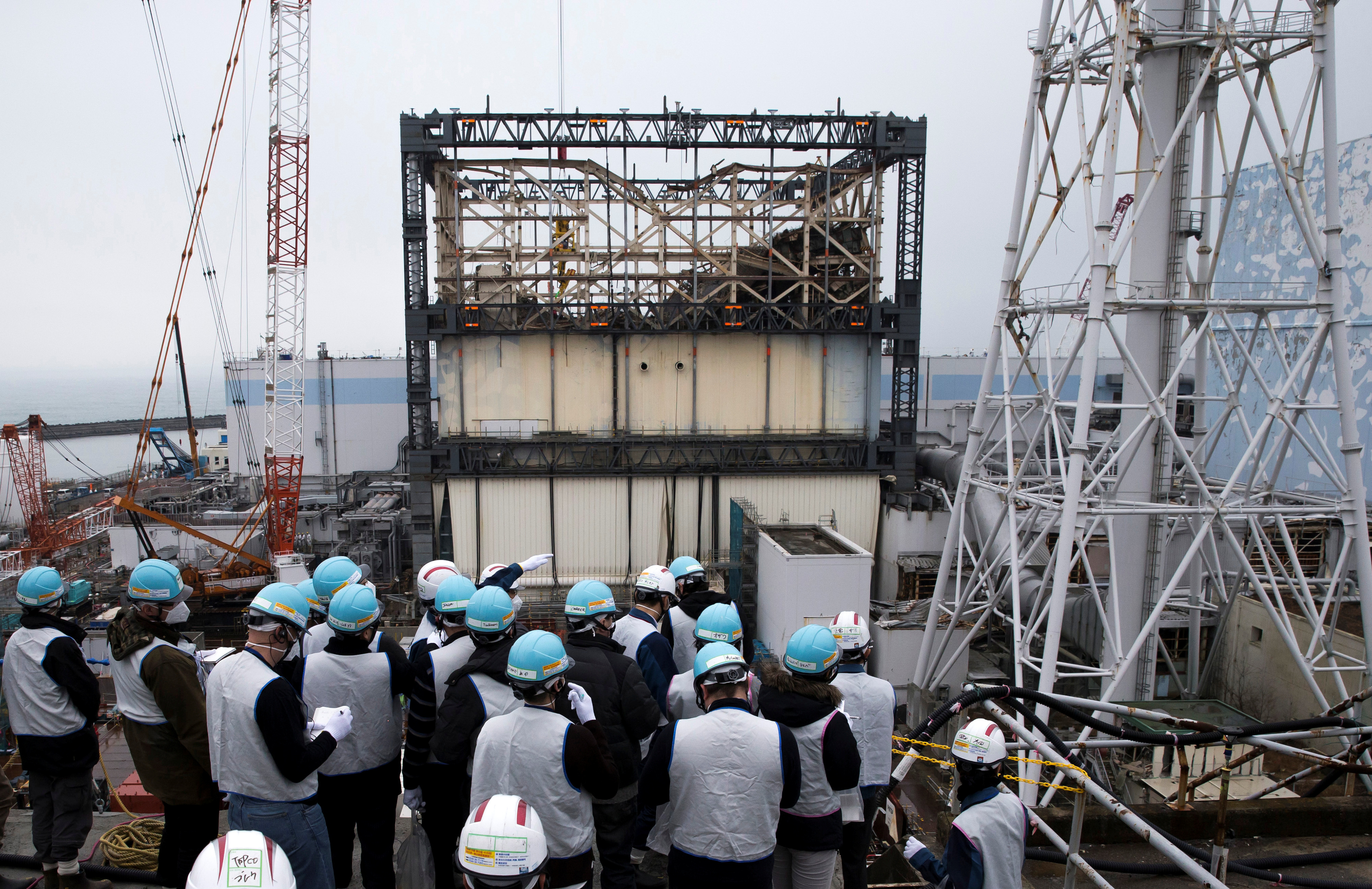 Members of the media look at the Unit 1 reactor building at TEPCO's Fukushima Dai-ichi nuclear power plant in Okuma, Fukushima