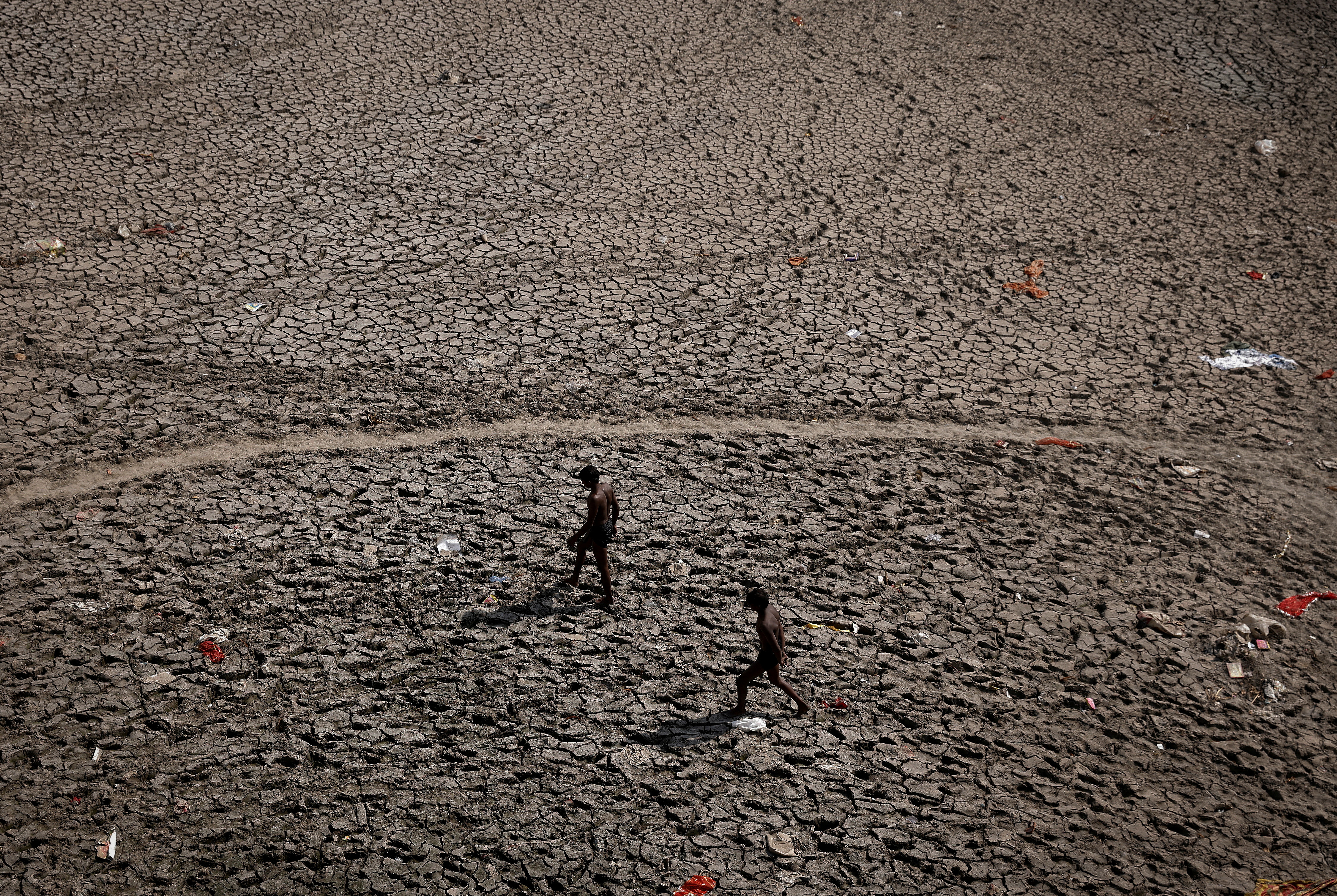 Men walk through an almost dry river bed of Yamuna after searching for recyclable material on a hot summer day in New Delhi