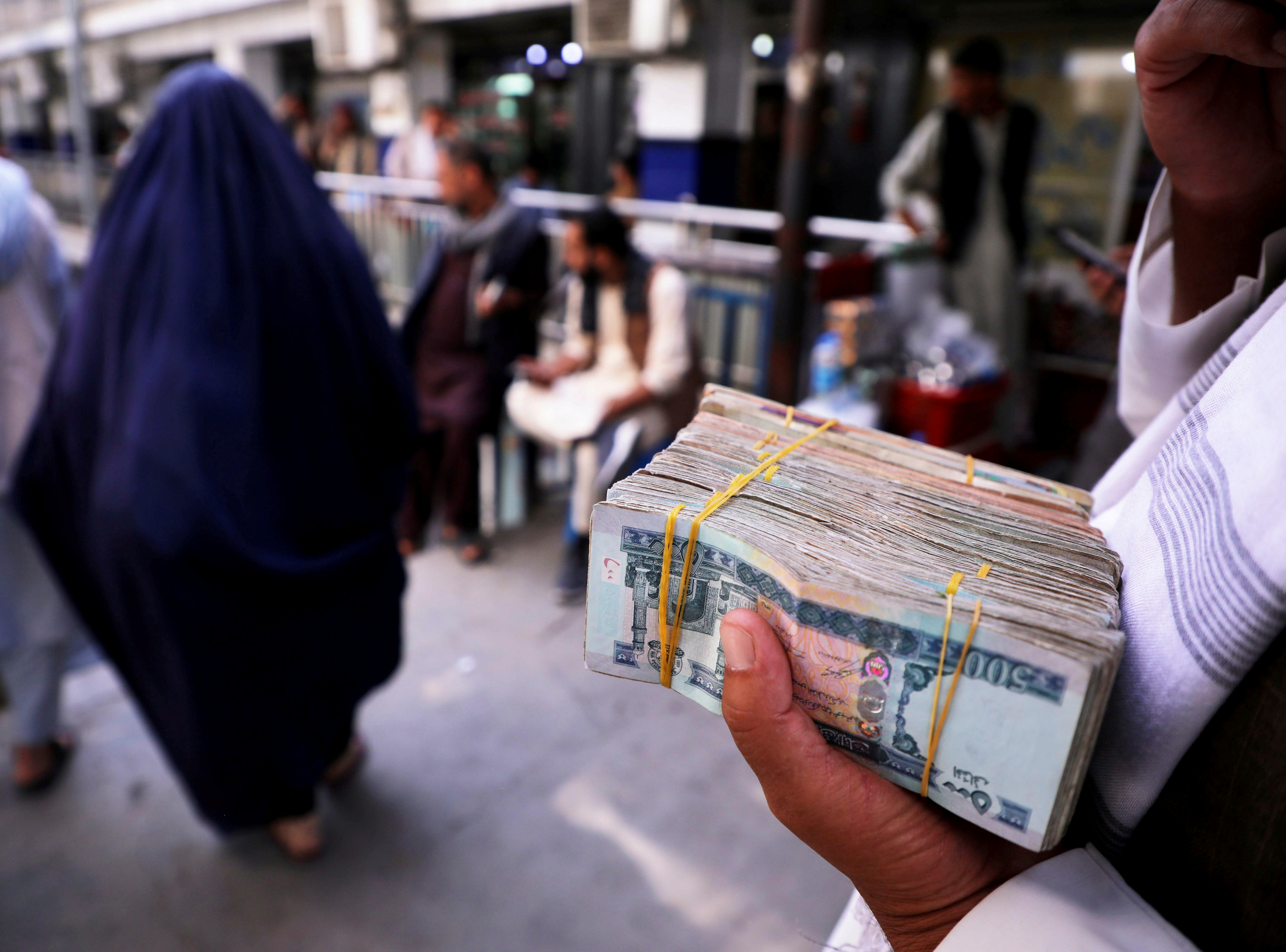 Person holds a bundle of Afghan afghani banknotes at a money exchange market in Kabul