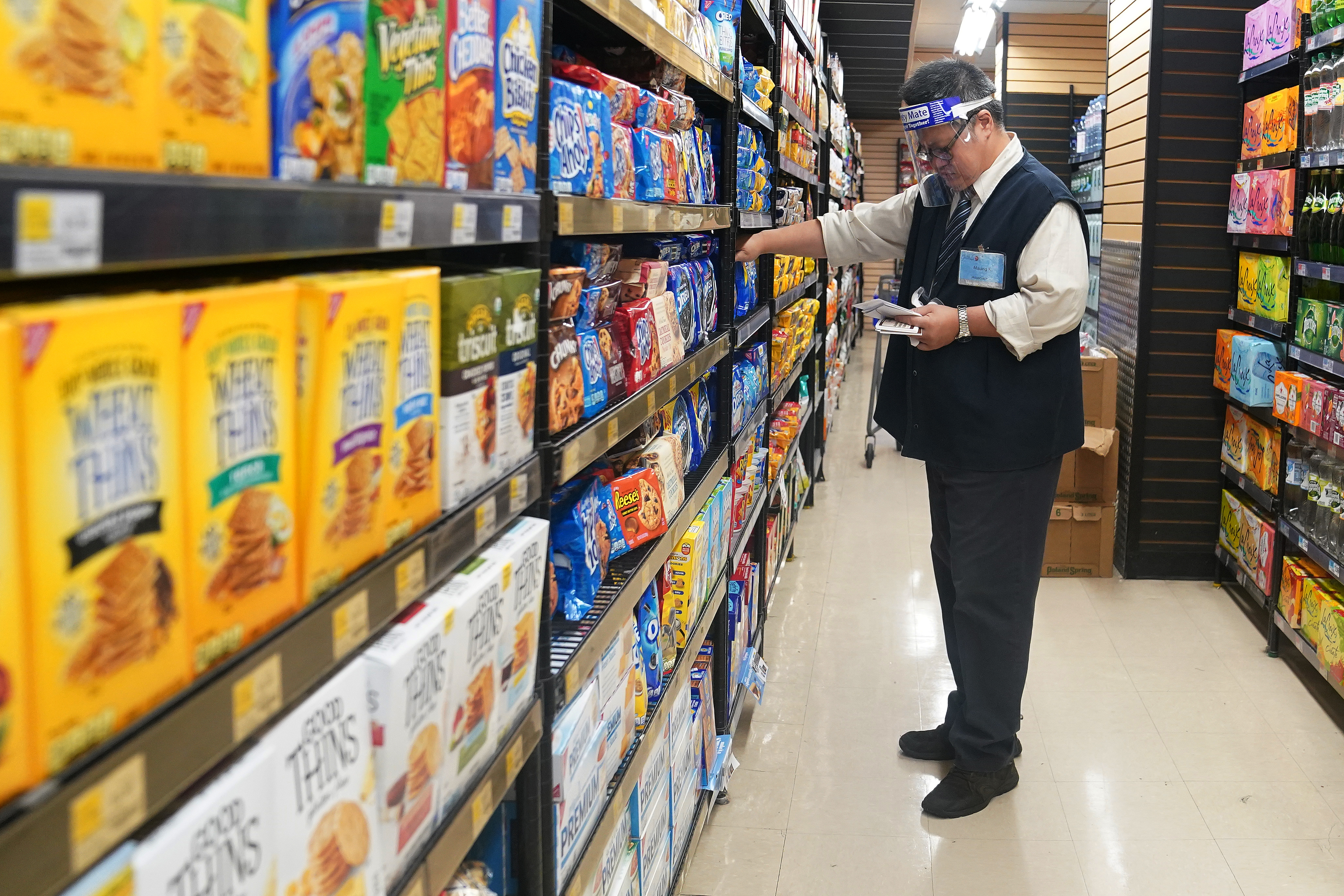 FILE PHOTO  - A worker with a face shield checks products on the shelf of a grocery store