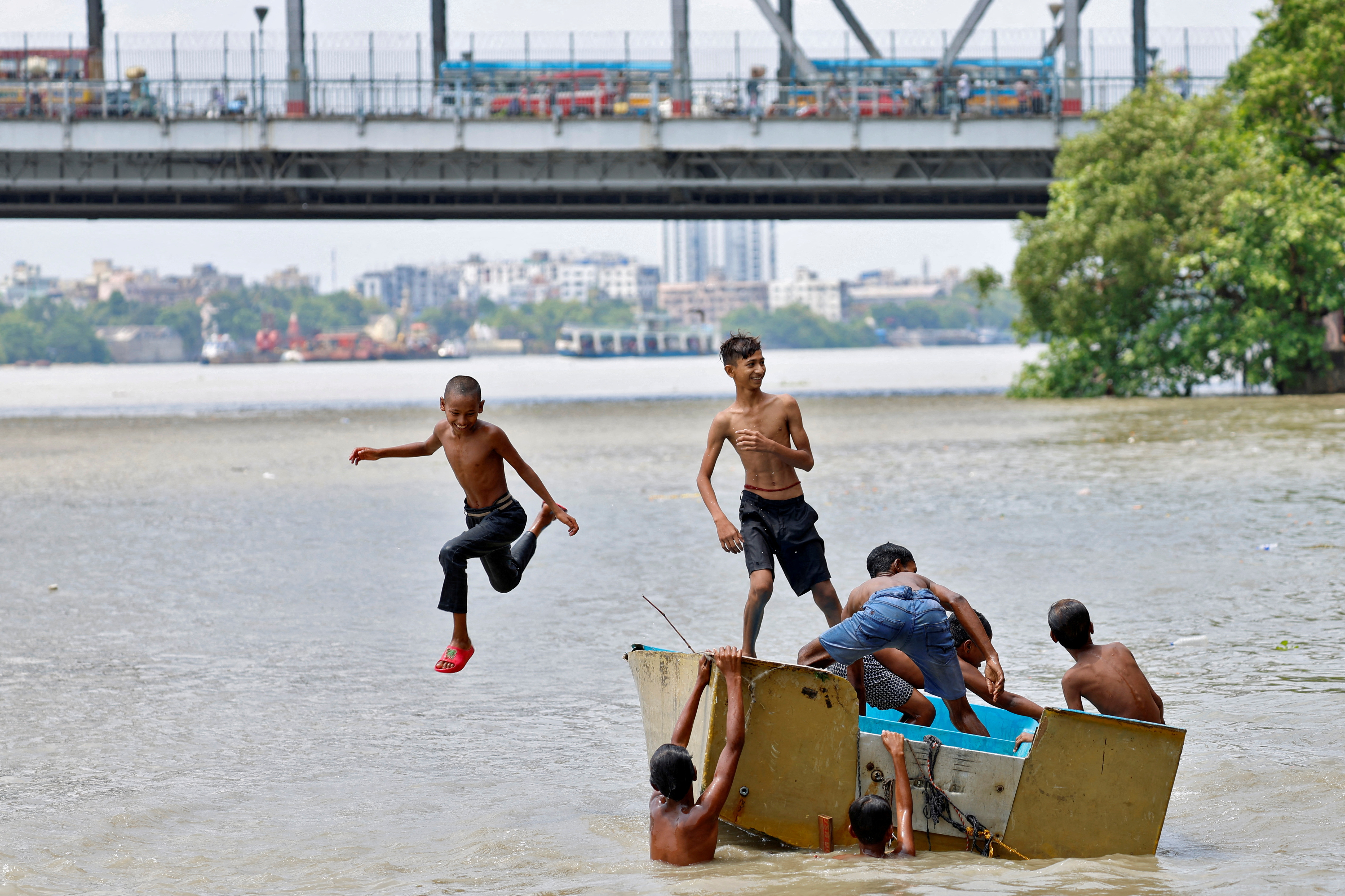 A boy jumps off a boat into the Ganges river to cool off on a hot summer day in Kolkata