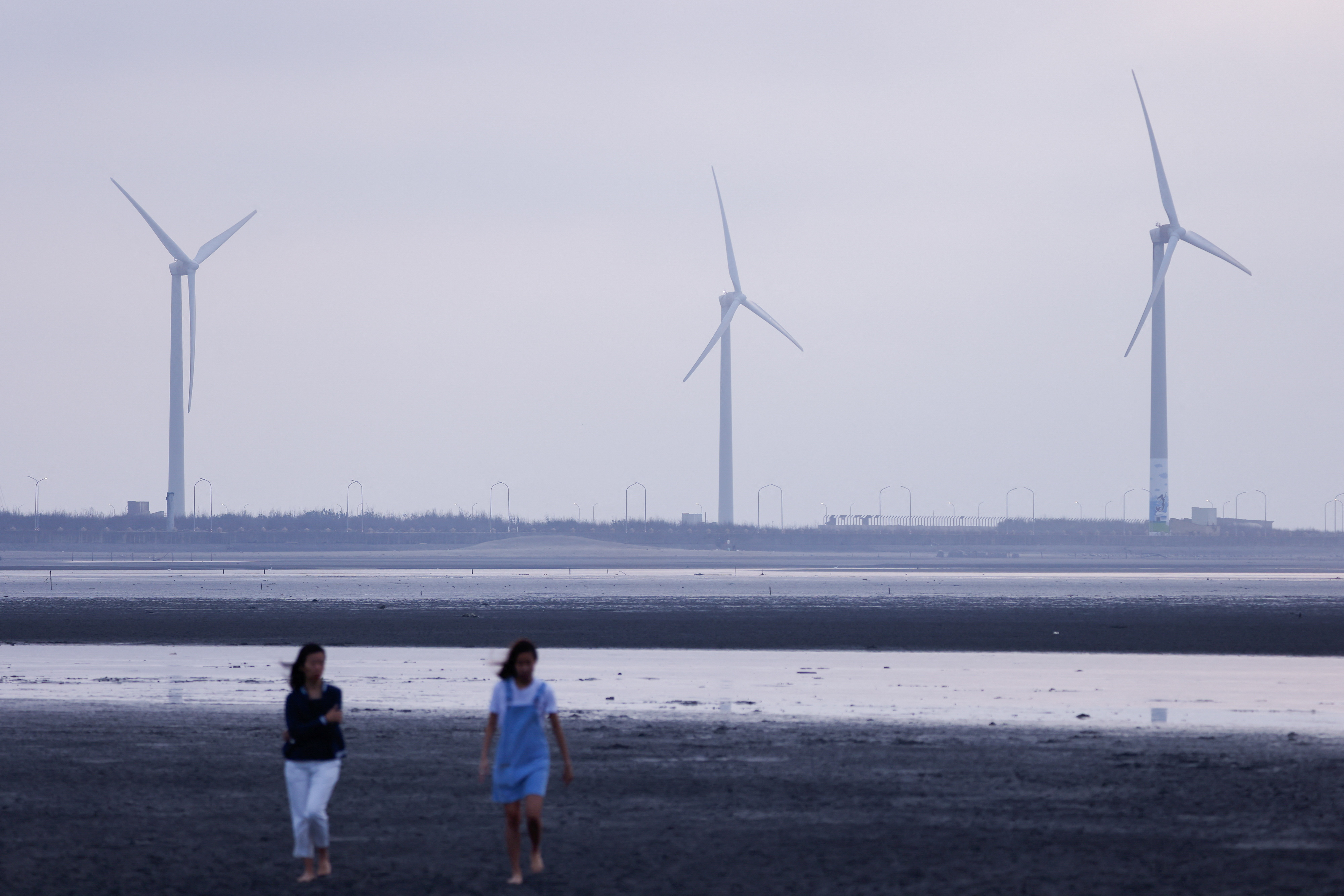 Tourists walk on the sand in front of wind turbines at Gaomei Wetlands in Taichung, in Taichung