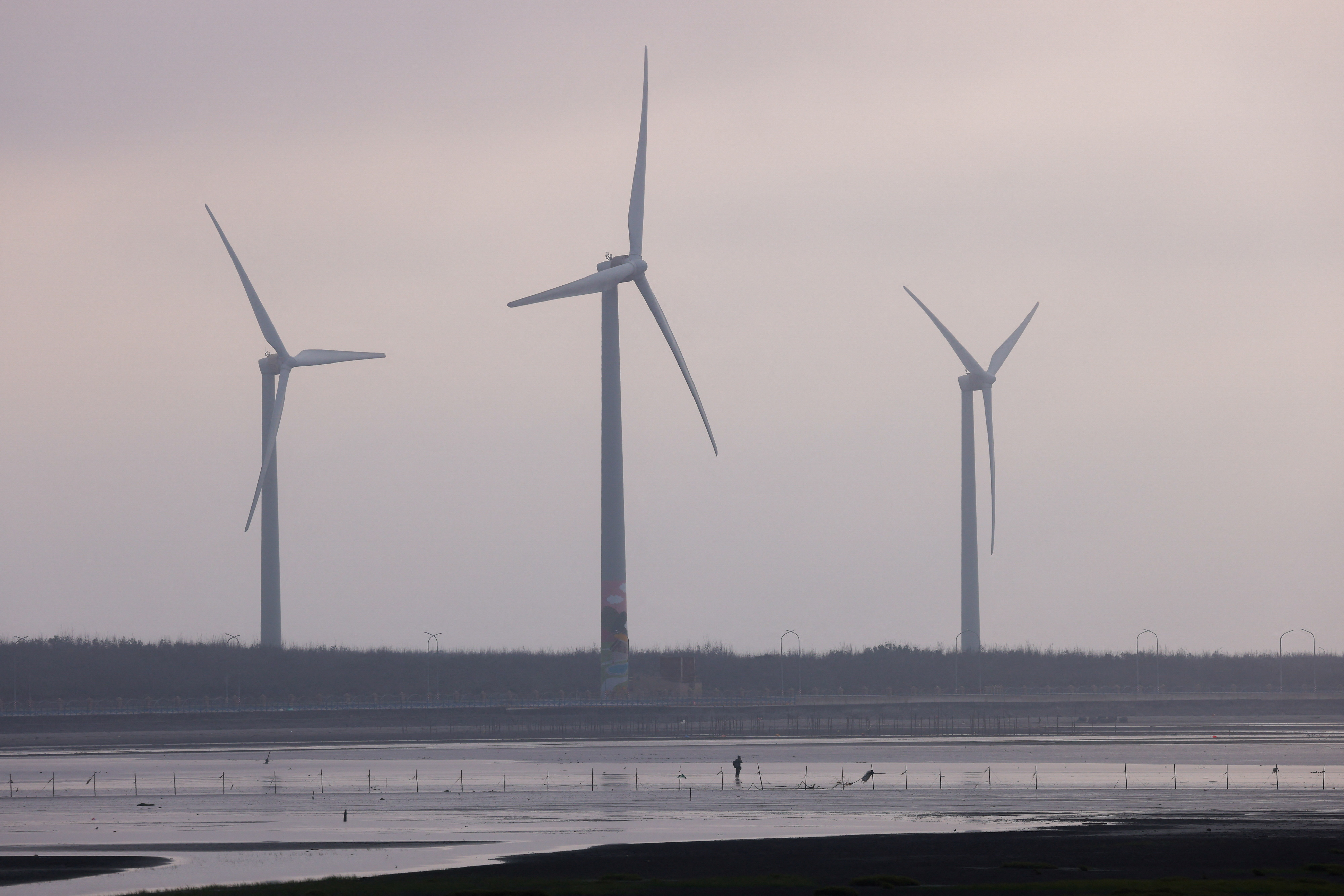 A fisherman walkes in front of wind turbines at Gaomei Wetlands in Taichung, in Taichung