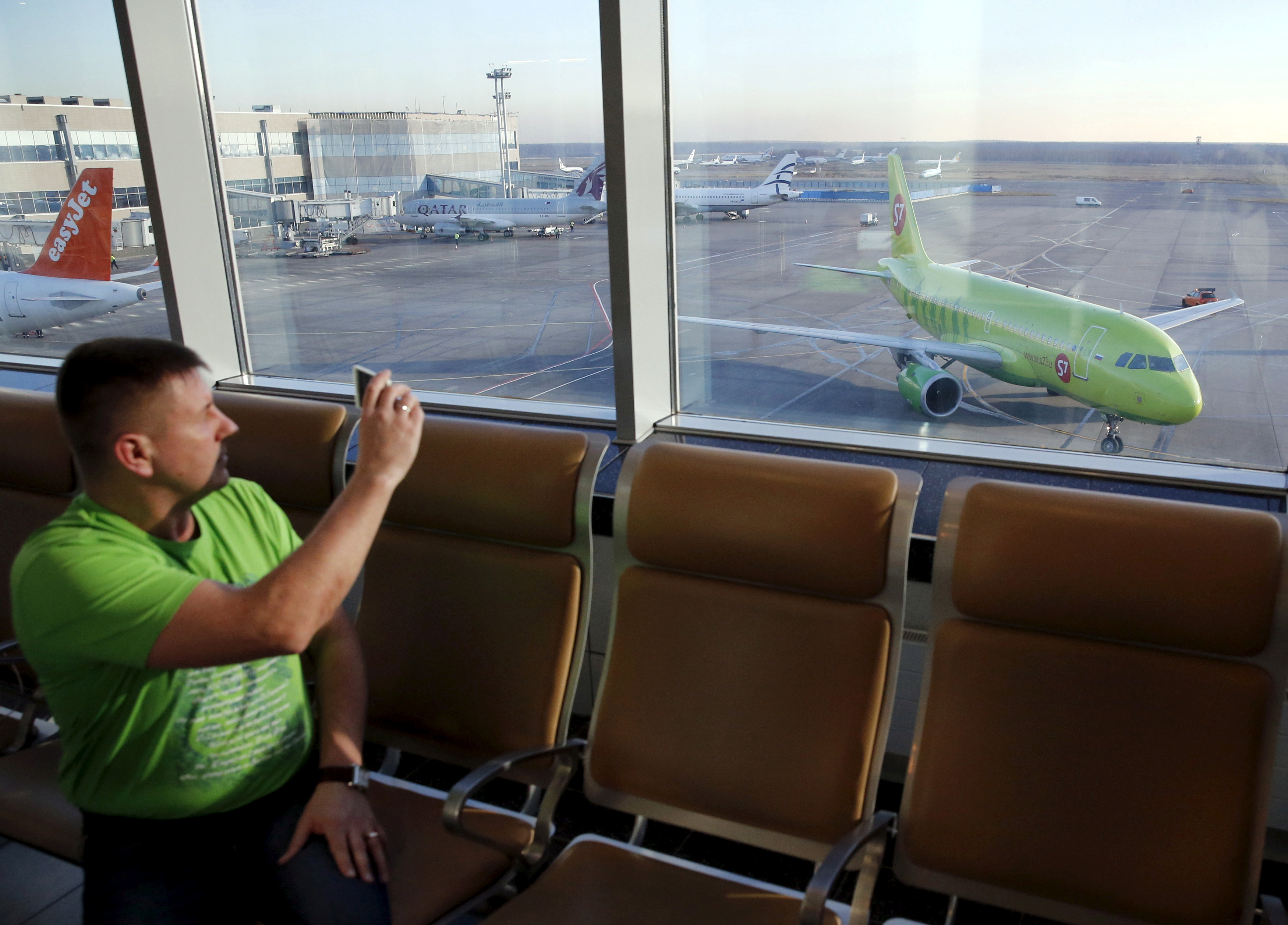 A man takes pictures, with a plane of S7 airlines seen in the background, at Domodedovo airport outside Moscow
