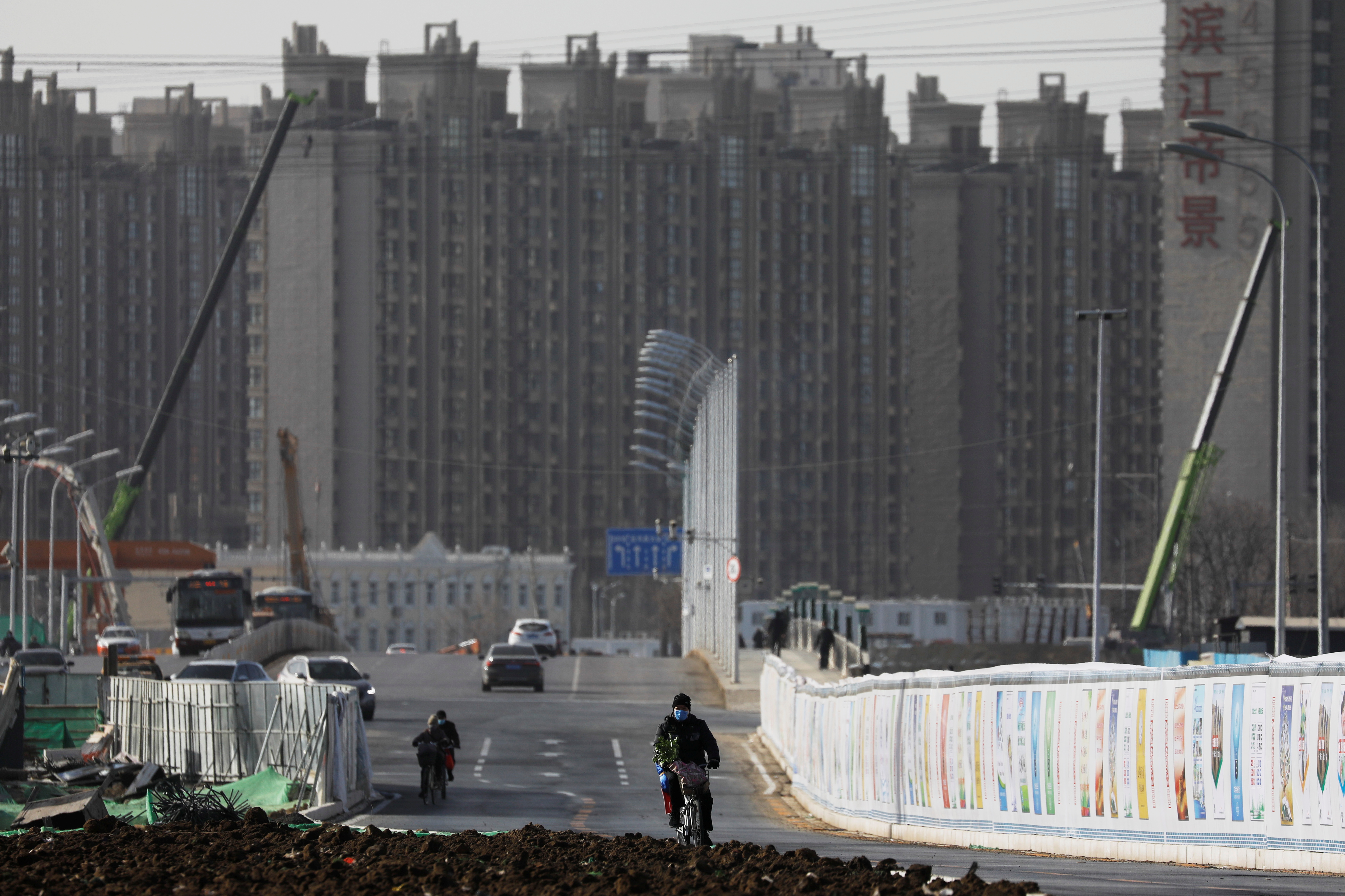 Man rides a bicycle next to a construction site near residential buildings in Beijing