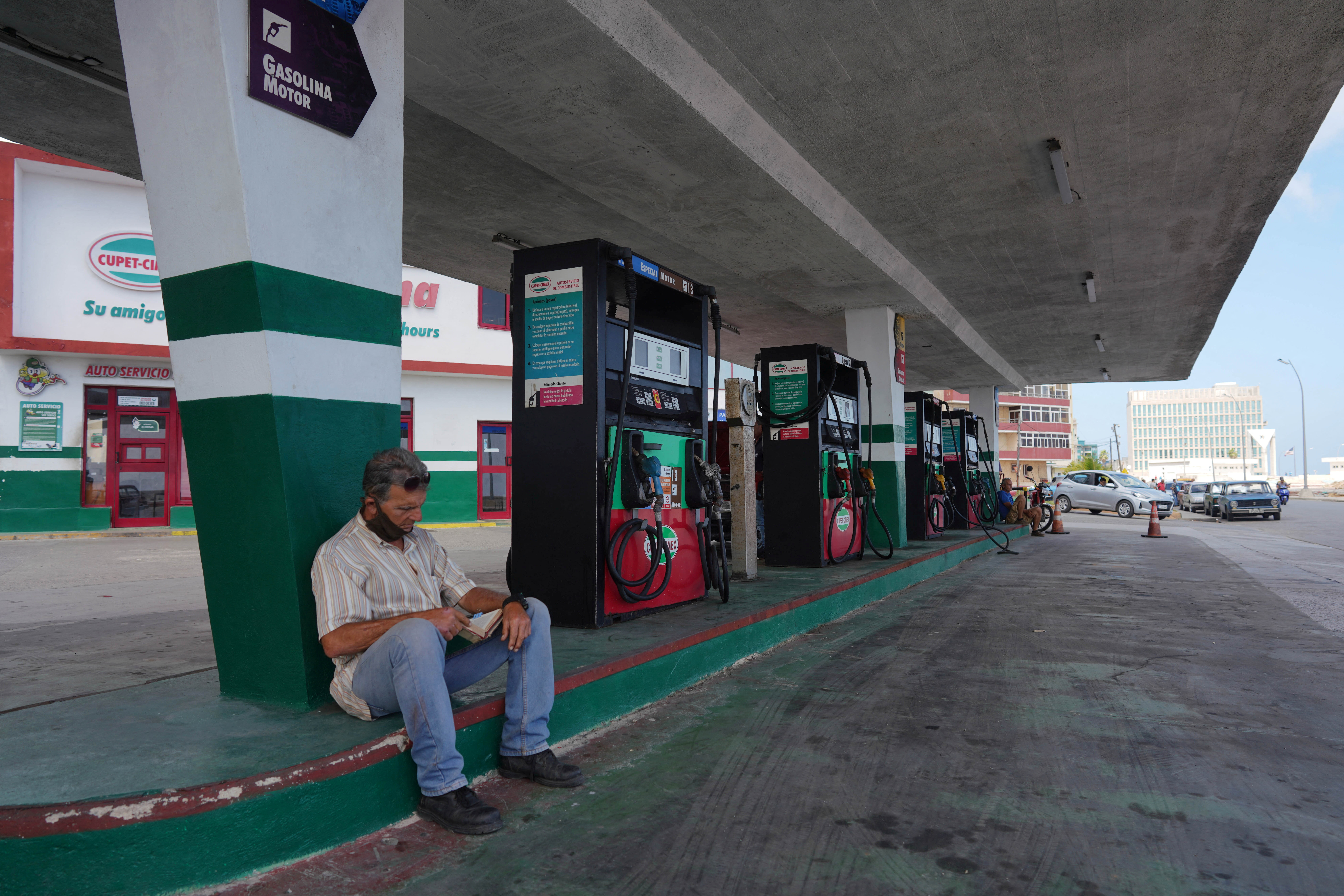Jose Mesejo, 65, reads a book as he waits for electricity to fill up the tank of his motorbike at a gas station in Havana