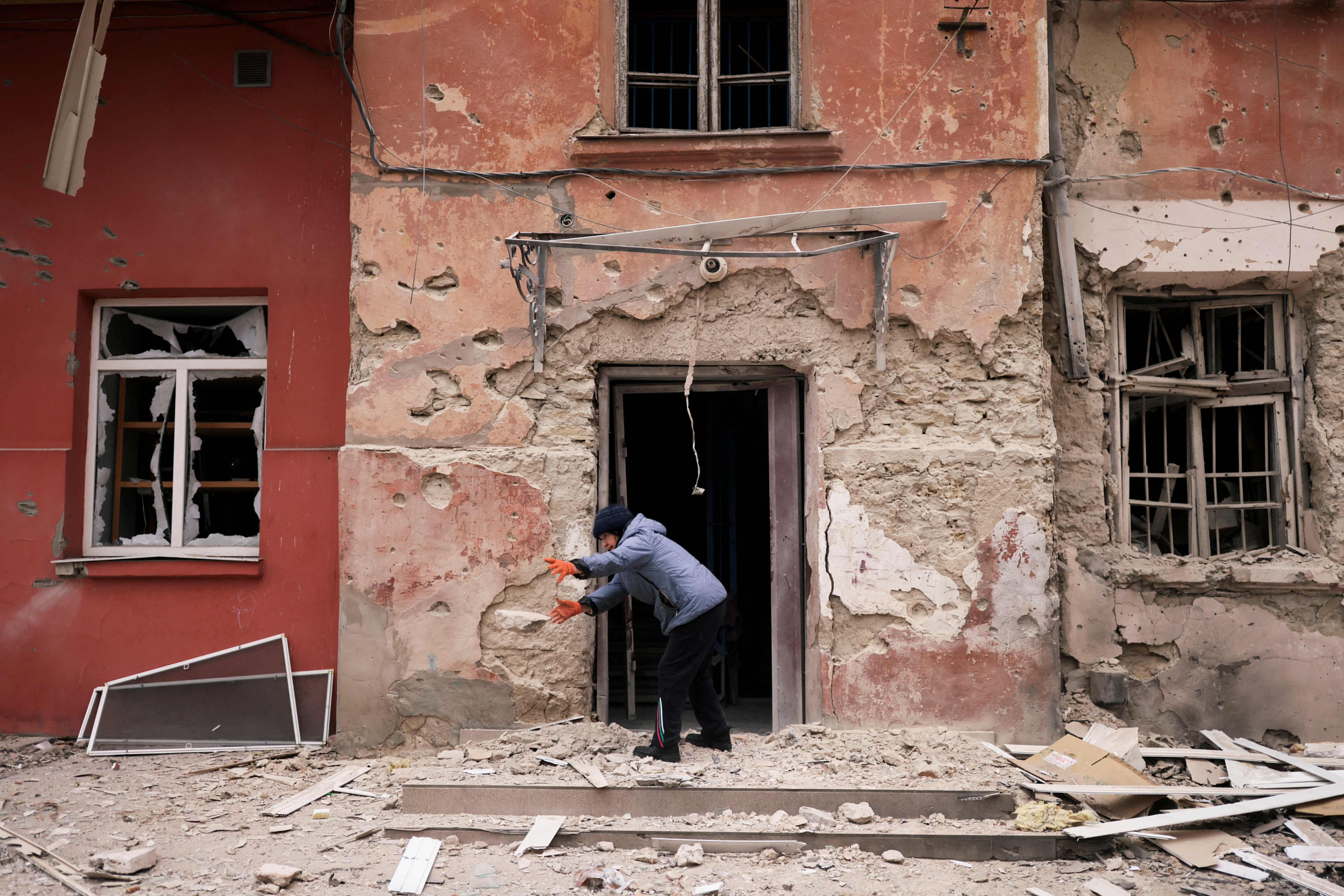 Zoya Mykolaivna removes debris in front of her apartment damaged by a Russian military strike in Kherson