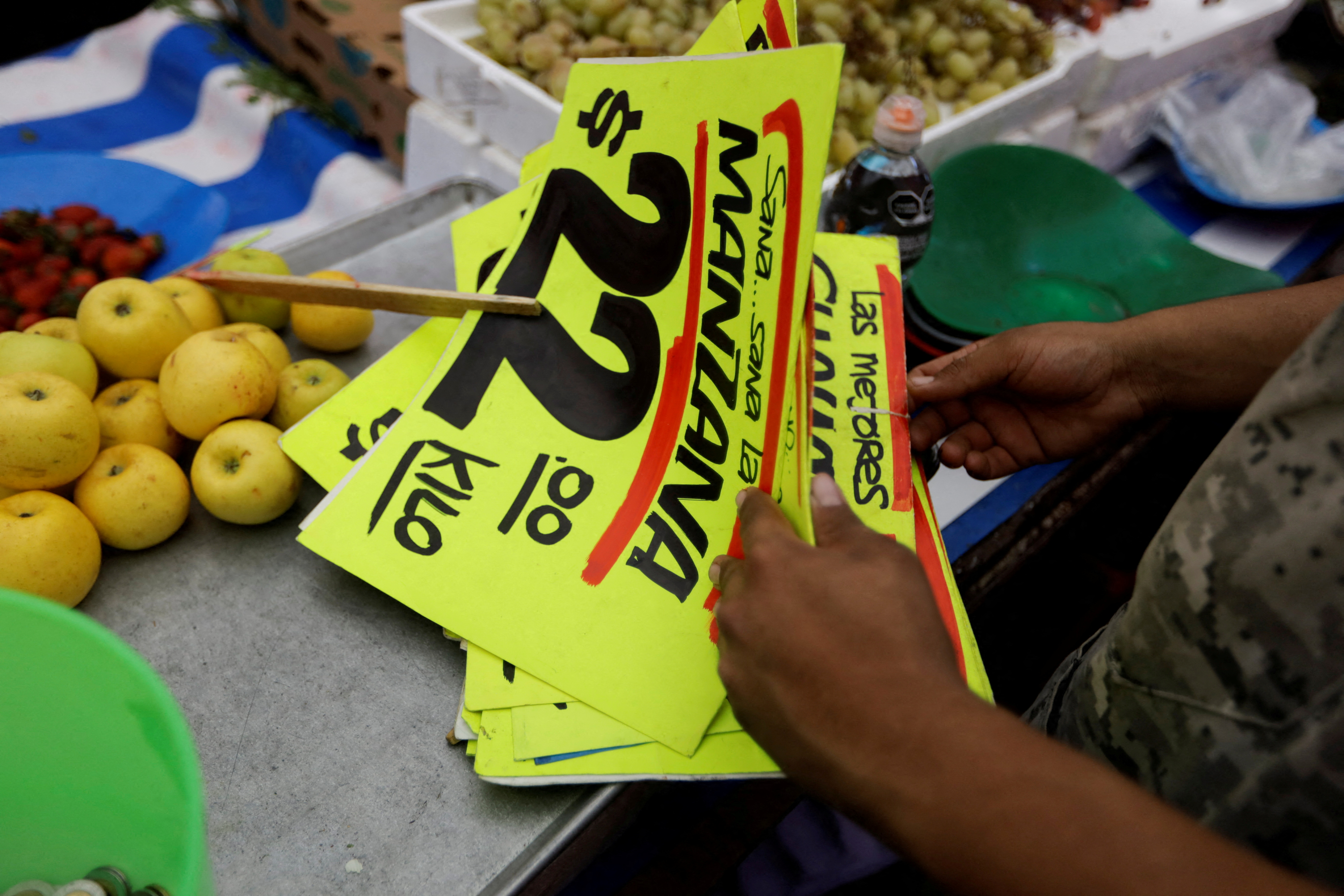 A vendor arranges signs displaying the prices of fruits in his stall at a street market, in Mexico City