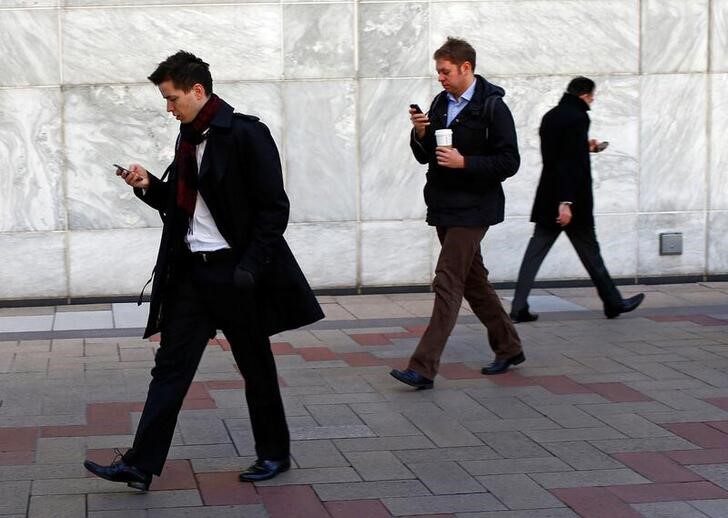 People look at their phones while walking at the Canary Wharf business district in London