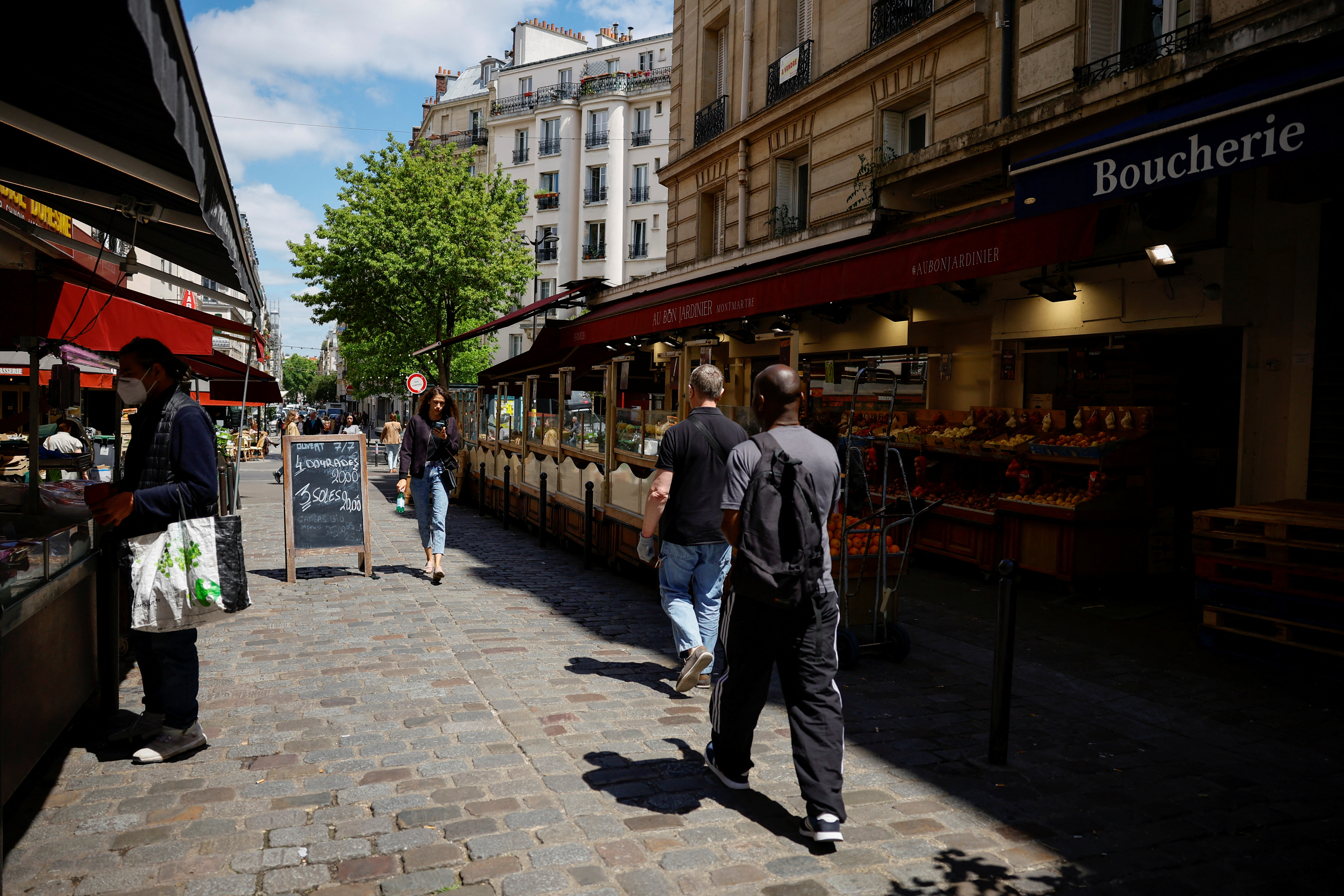 People walk past food shops on a street in Paris