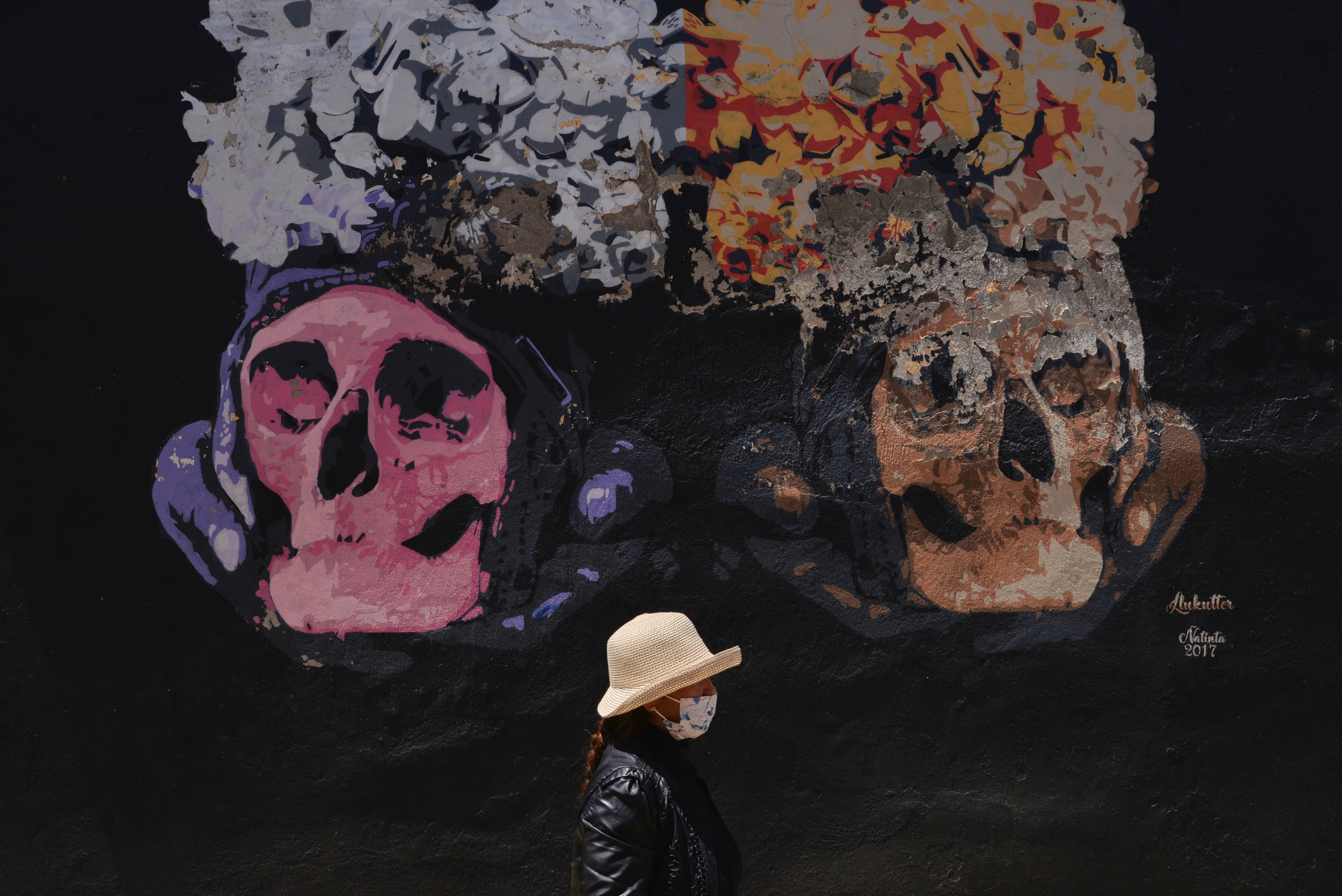 A woman walks in front of a mural of skulls during the celebration of the Day of Skulls, a tradition rooted in ancient indigenous beliefs meant to bring good fortune and protection by honoring the dead, at a cemetery in La Paz, Bolivia, November 8, 2021. REUTERS/Sara Aliaga  