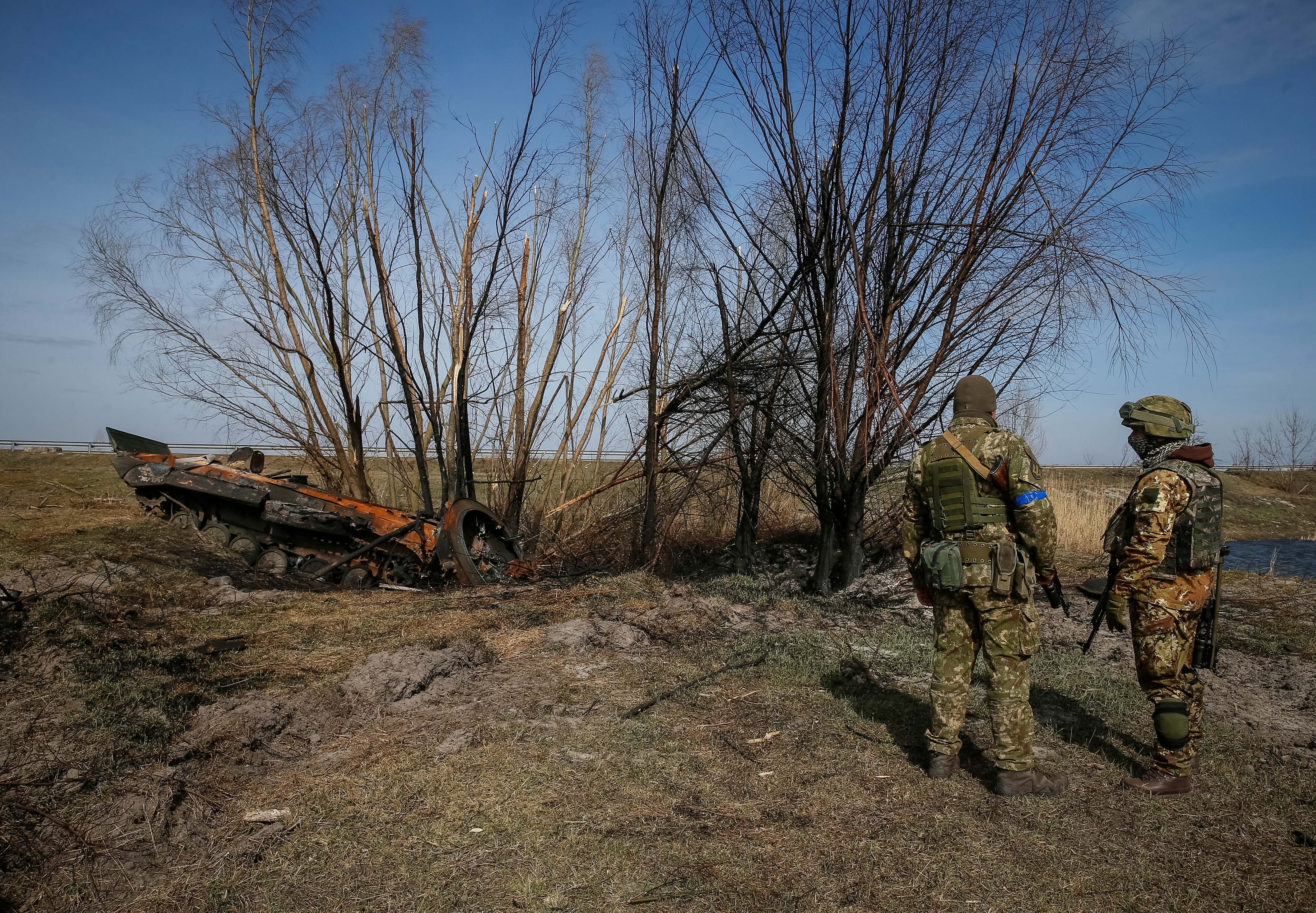 Ukrainian servicemen stand near the wreck of a Russian Armoured Personnel Carrier on the front line in the Kyiv region