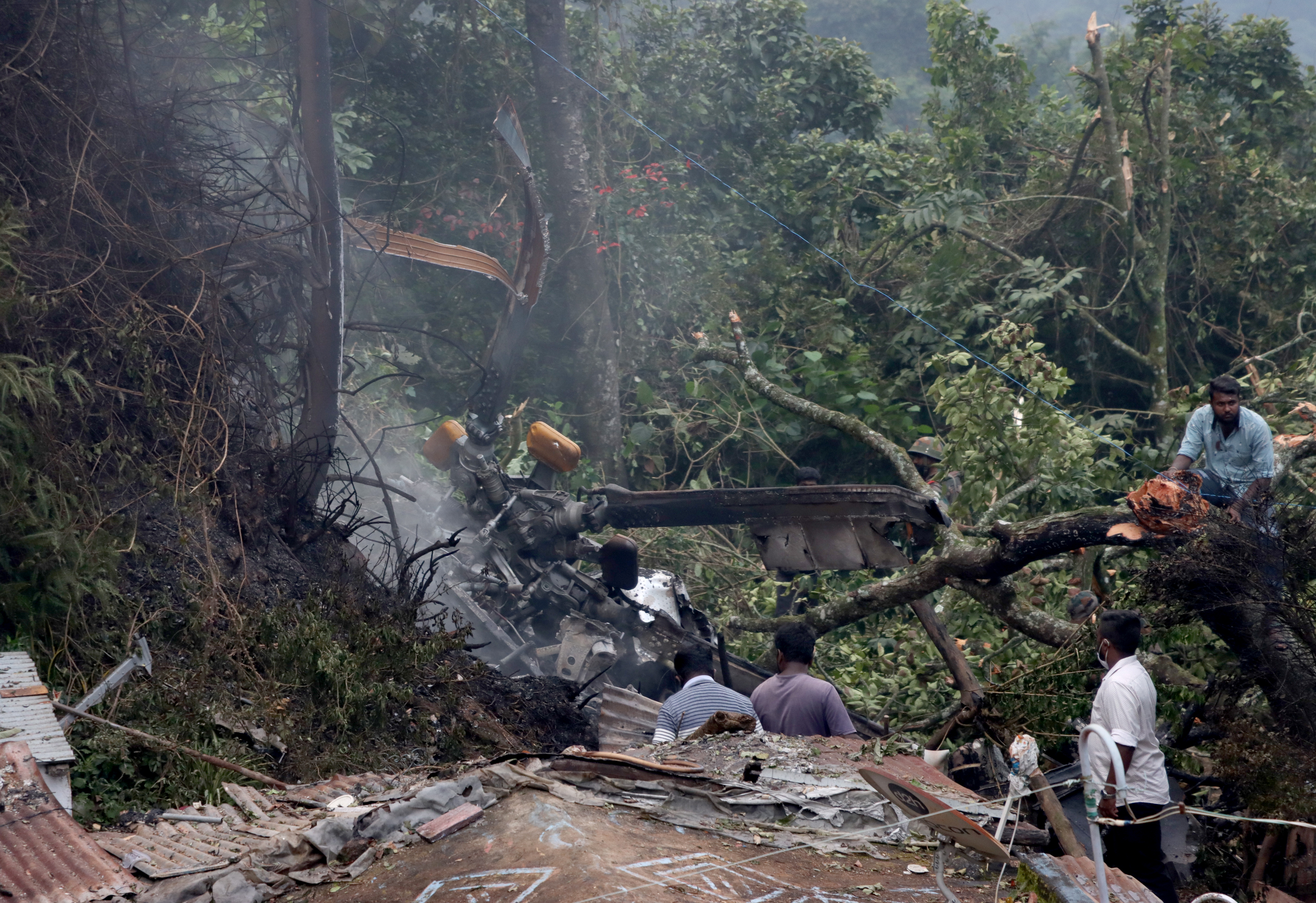 People stand near the debris of the Russian-made Mi-17V5 helicopter after it crashed near the town of Coonoor in the southern state of Tamil Nadu, India, December 8, 2021. REUTERS/Stringer