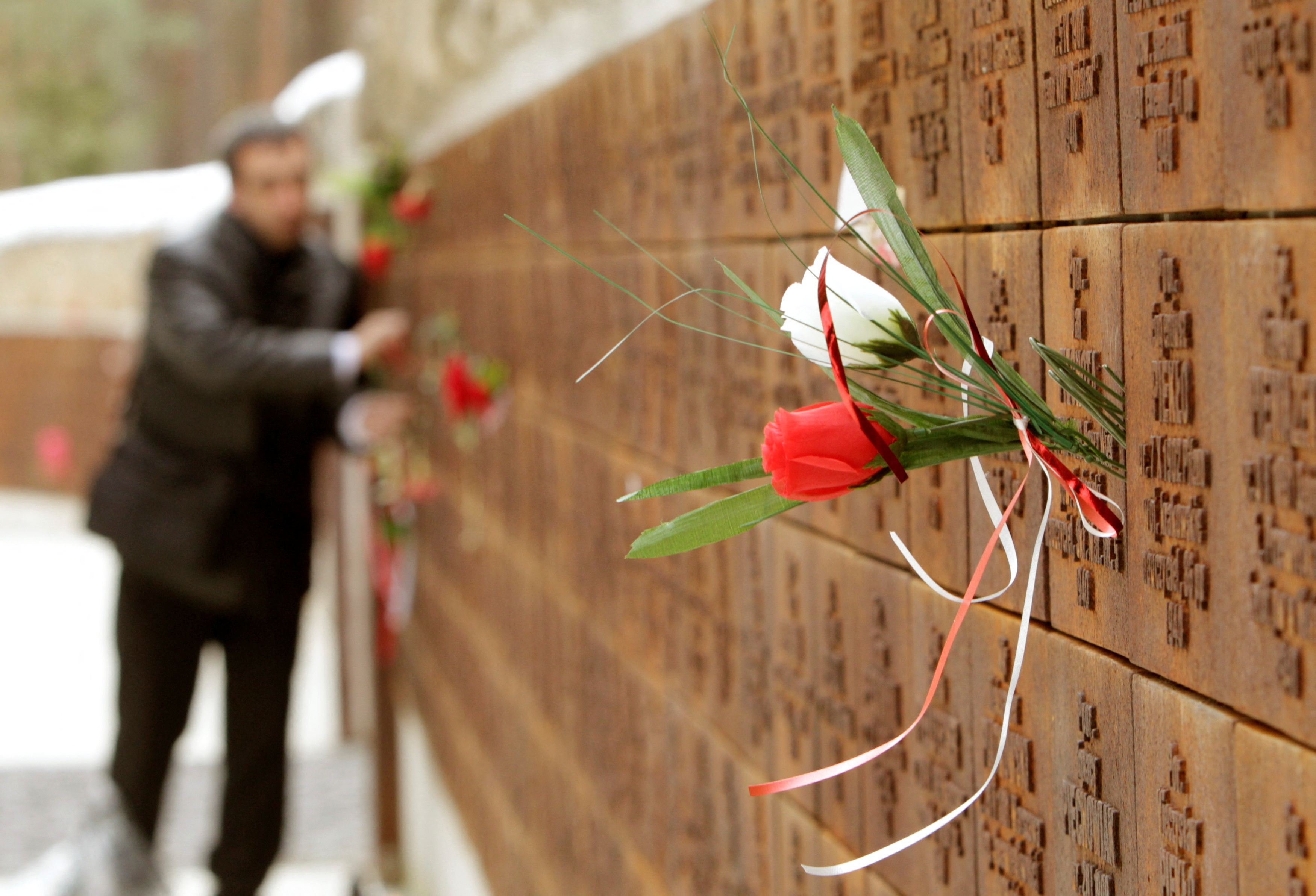 A man puts flowers into a wall with names of killed Polish officers during a commemoration ceremony at a memorial complex in Katyn