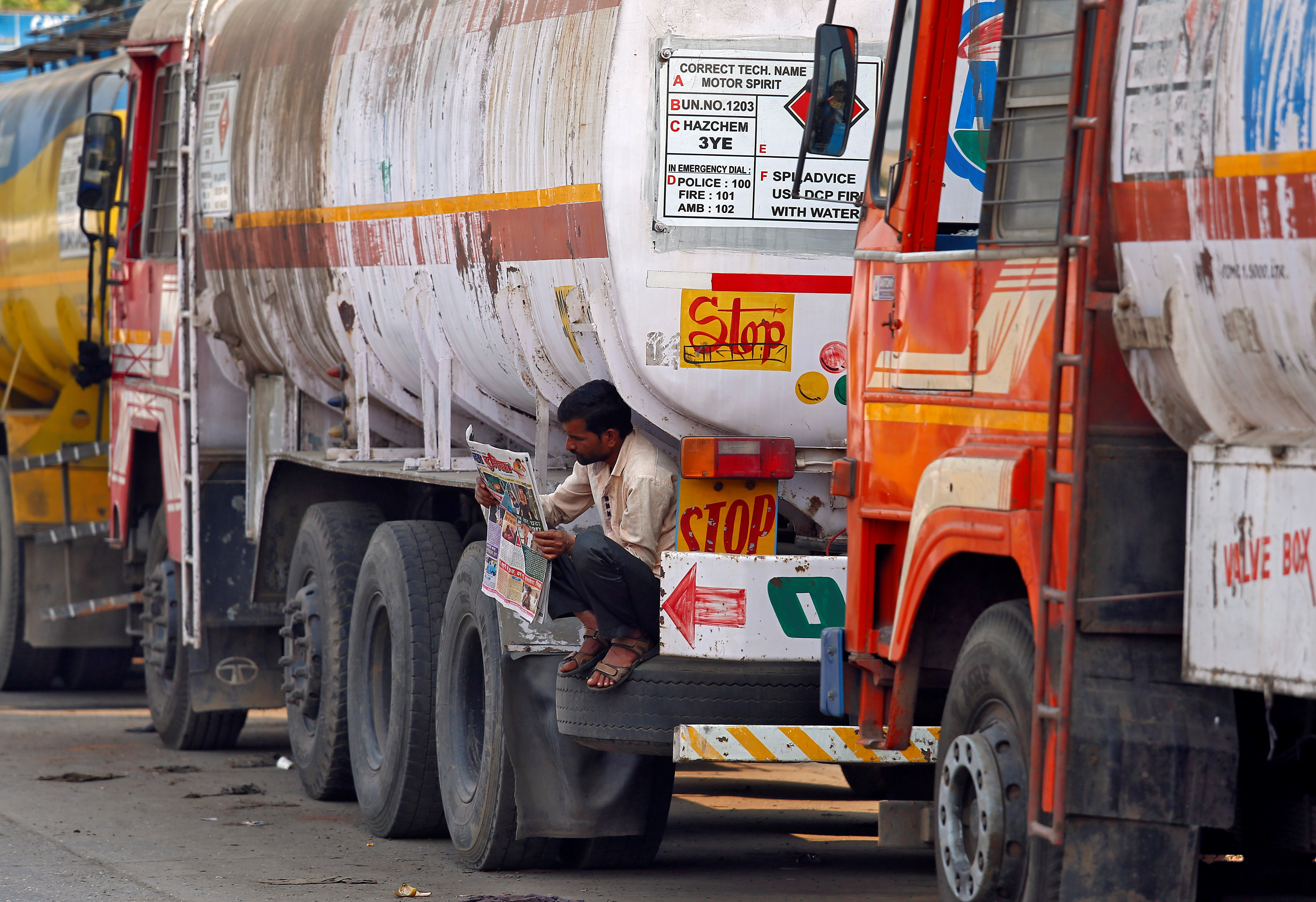 A driver reads a newspaper as he sits on a spare tire attached to a parked oil tanker at a truck terminal in Mumbai