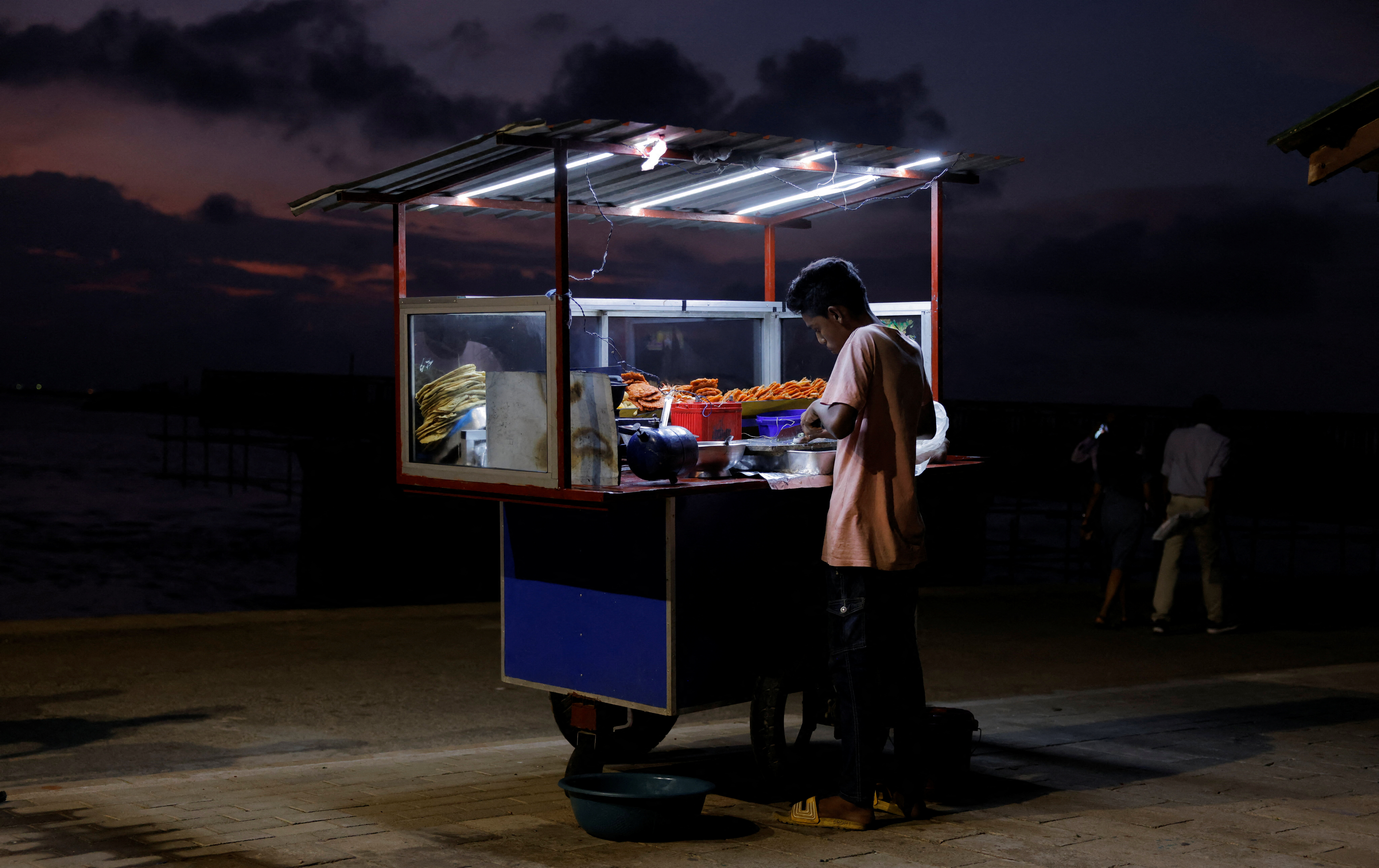 A vendor cooks food for customers in his food cart at Galle Face Green, in Colombo