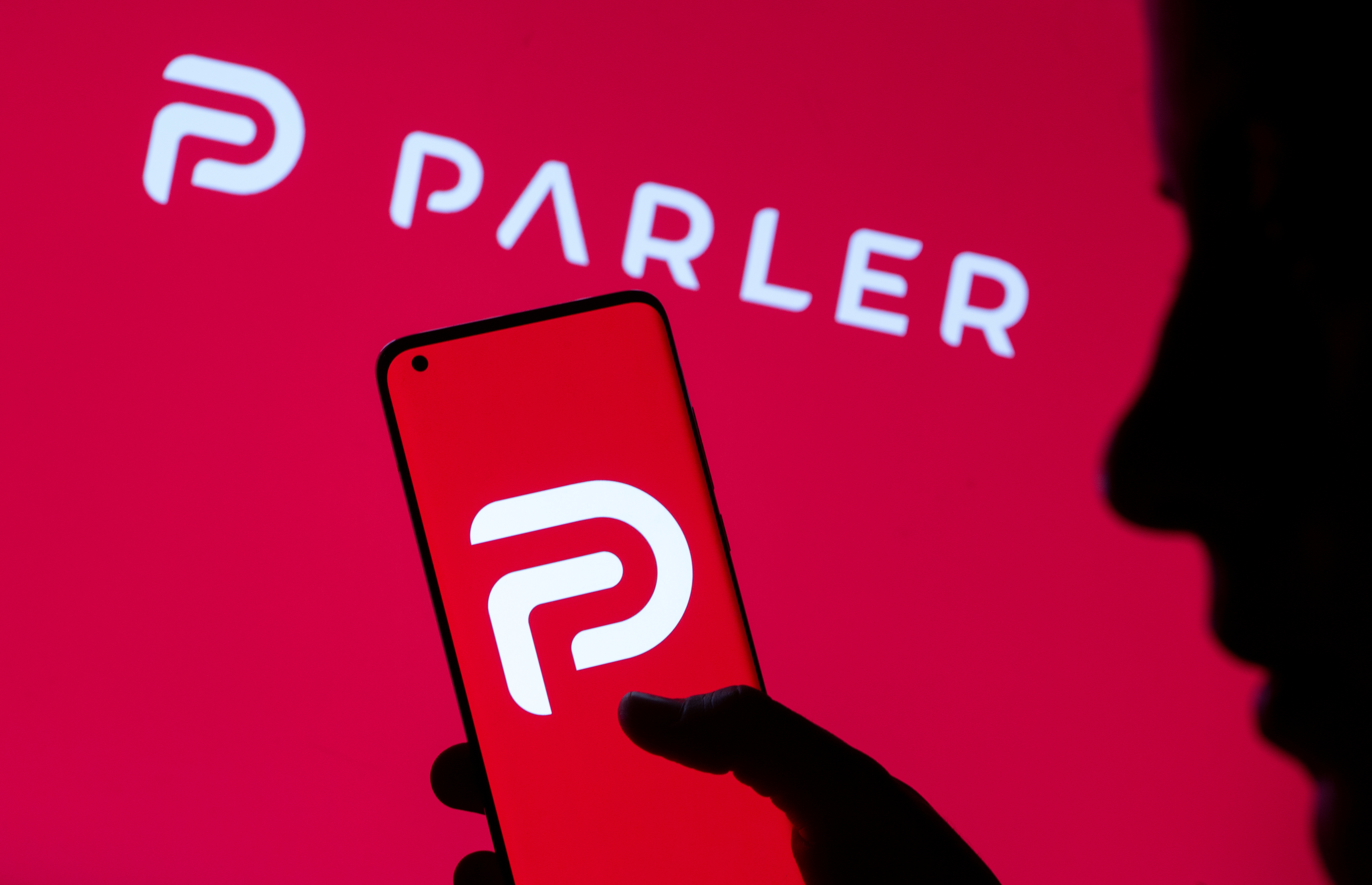 Woman holding smartphone with Parler logo in front of displayed same logo in this illustration