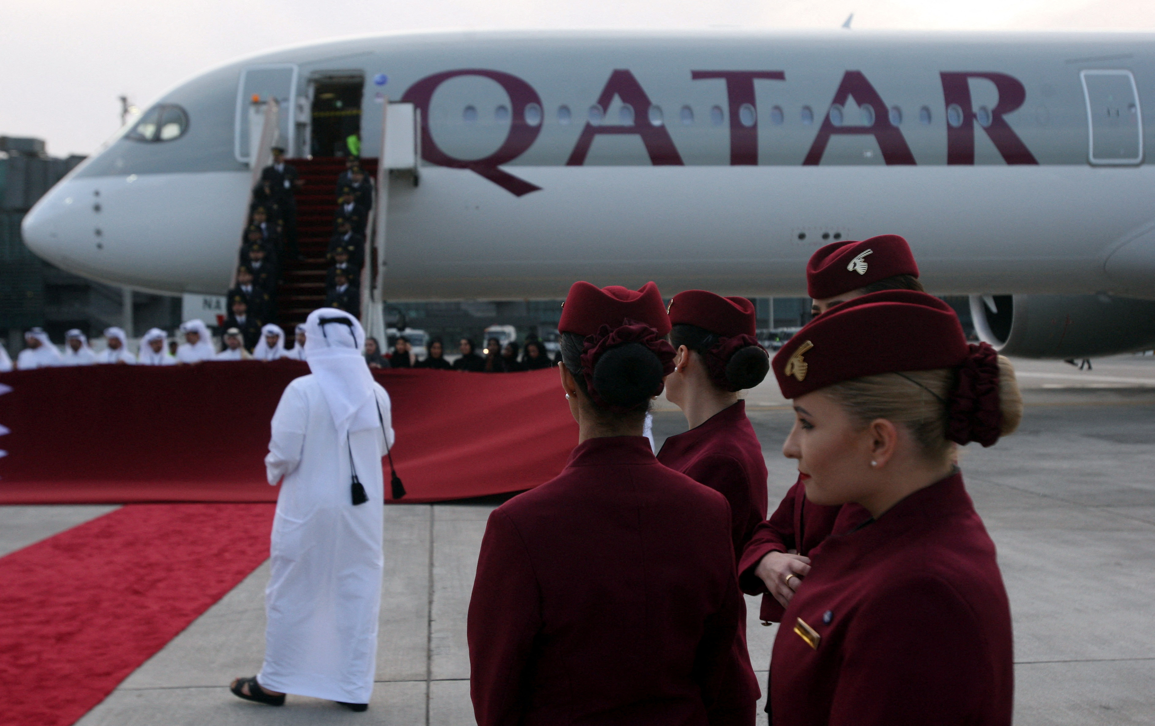 Qatar Airways cabin crew stand in front of an Airbus A350-1000 at Hamad International Airport in Doha