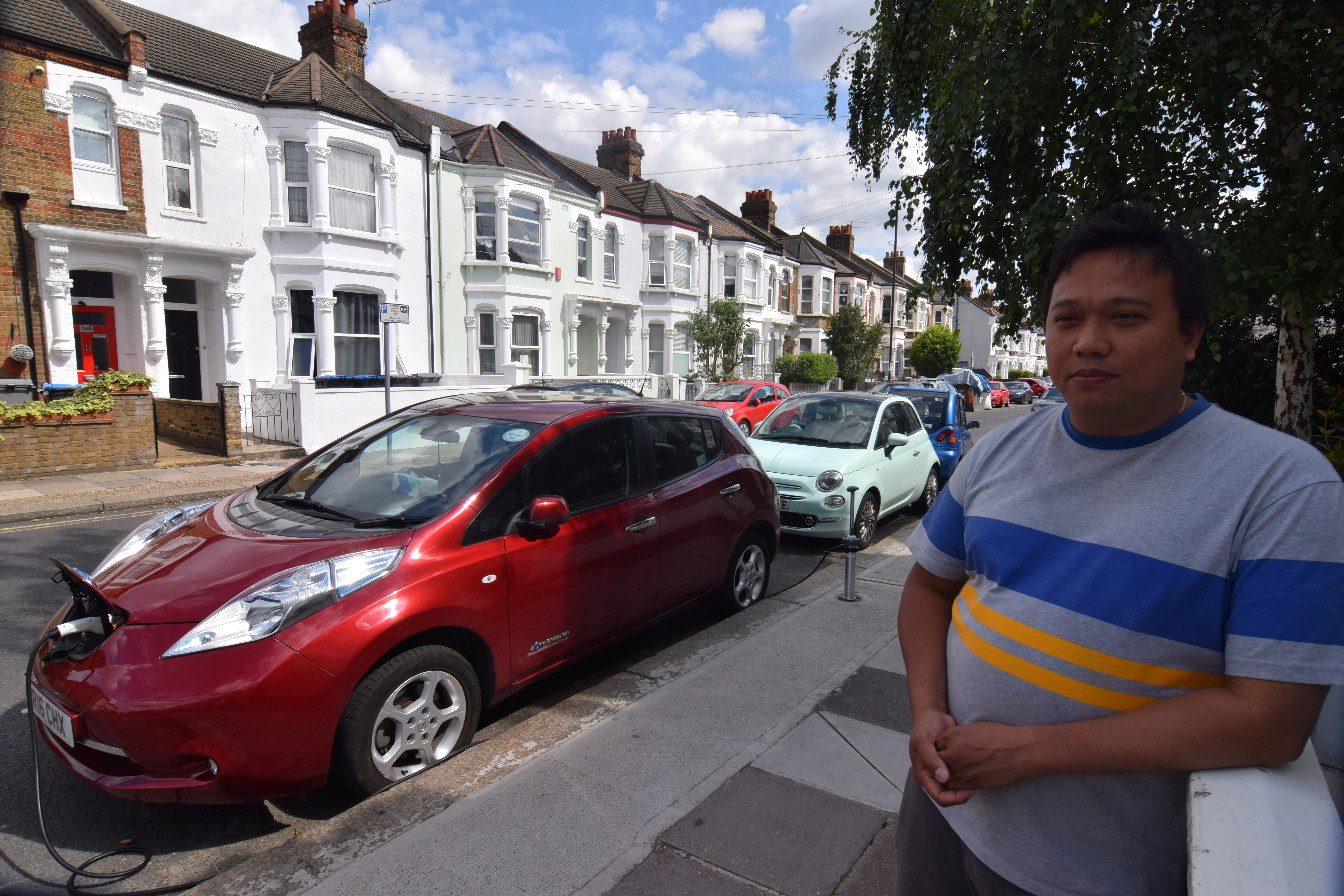 Uber driver Tim Win poses for a photo with his fully-electric Nissan Leaf, plugged into an on-street residential electric vehicle charging system developed by startup Trojan Energy, in London