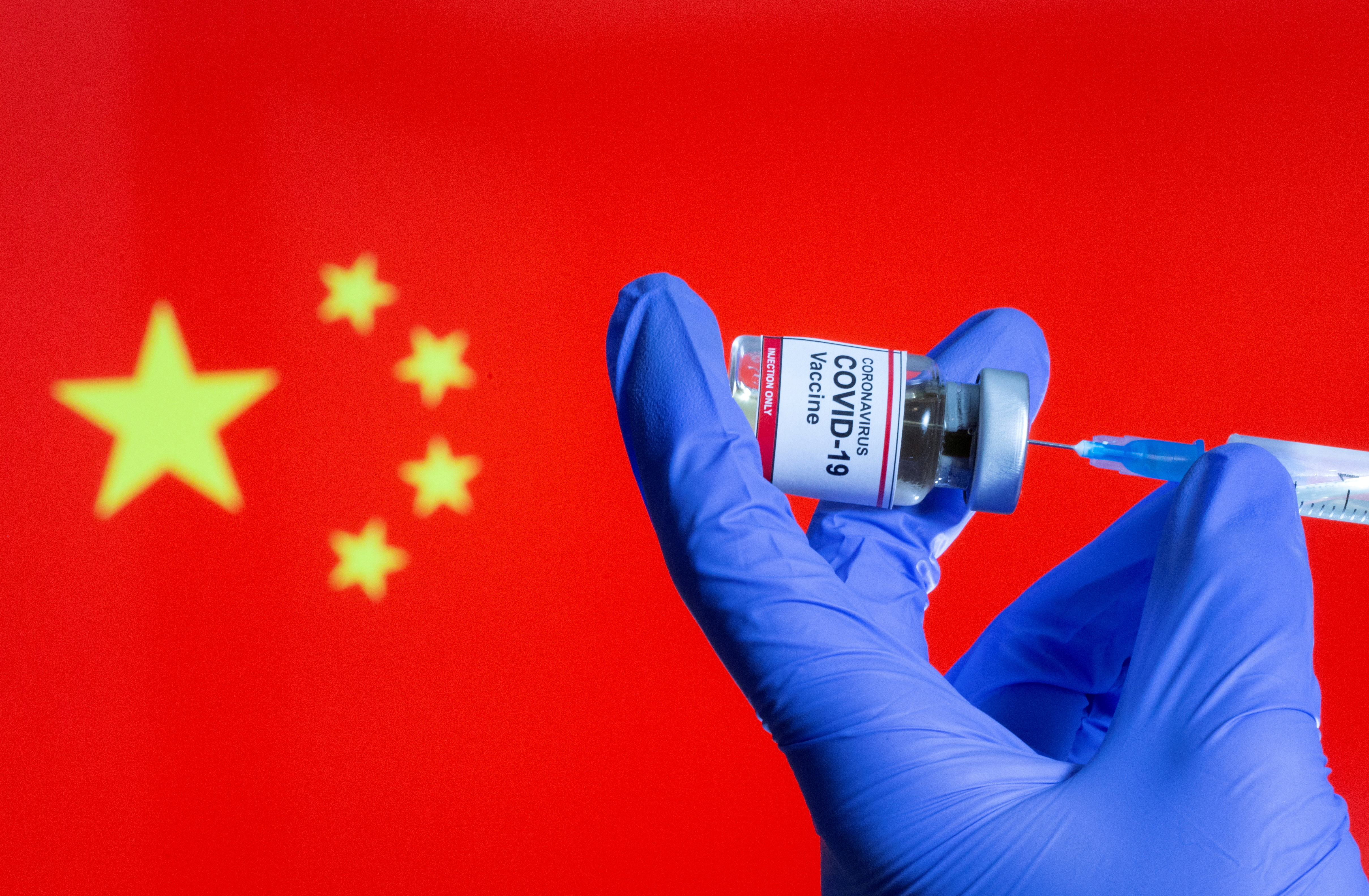 A woman holds a small bottle labeled with a "Coronavirus COVID-19 Vaccine" sticker and a medical syringe in front of displayed China flag in this illustration